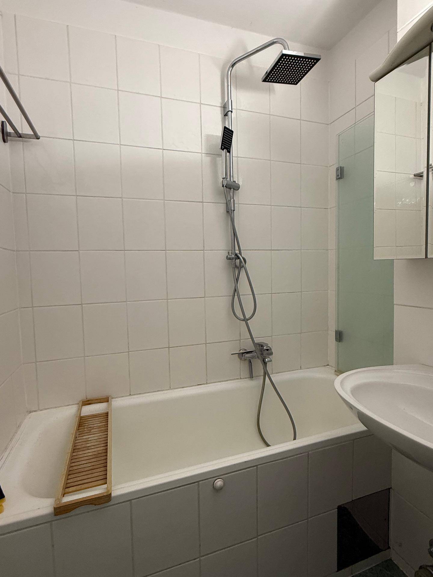 Badezimmer mit Badewanne, Duschfunktion und Waschbecken, ausgestattet mit weißen Fliesen.