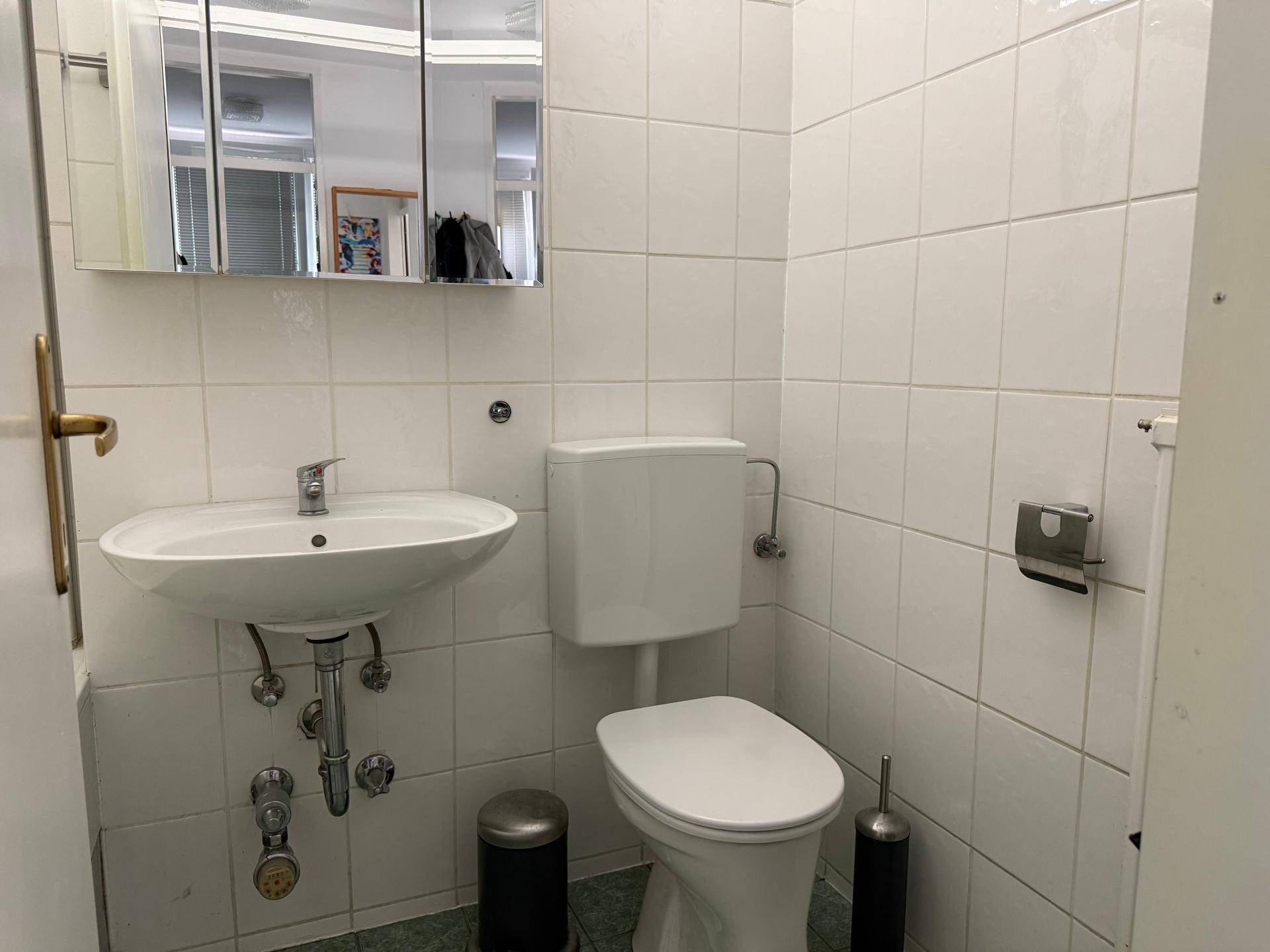 Separates WC mit Toilette, Waschbecken und Spiegelschrank, vollständig gefliest.