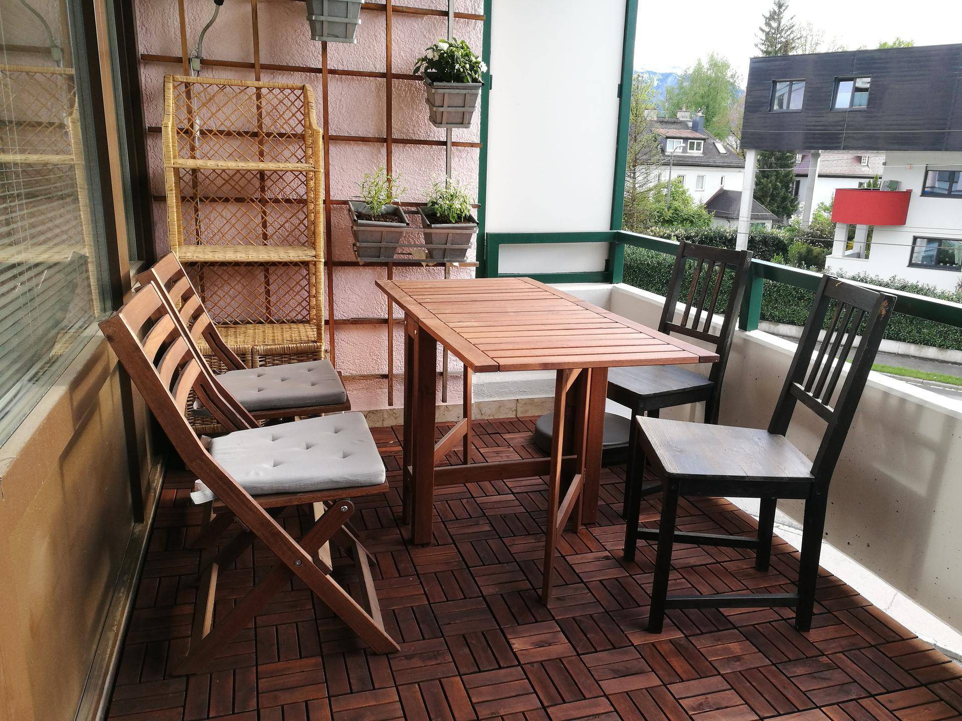 Möblierter Balkon mit Holzbodenfliesen, Esstisch und Stühlen, ideal für entspannte Stunden im Freien.
