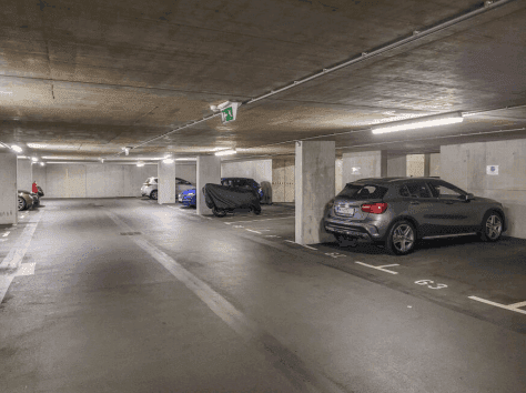 Geräumige und gut beleuchtete Tiefgarage mit mehreren geparkten Fahrzeugen und Betonwänden.