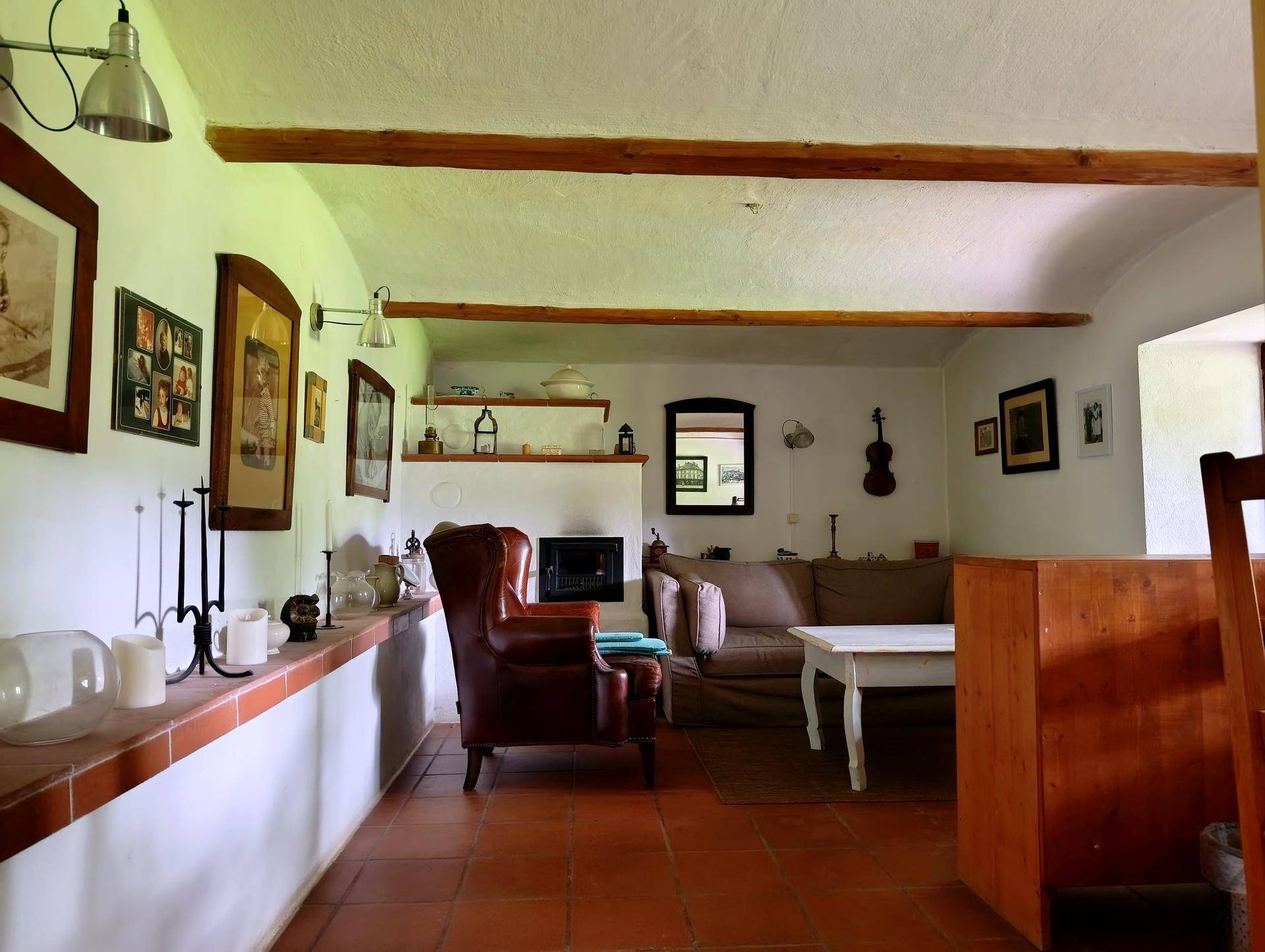 Geräumiges Wohnzimmer mit traditionellem Kamin, Terrakottafliesen und Holzbalken an der Decke.