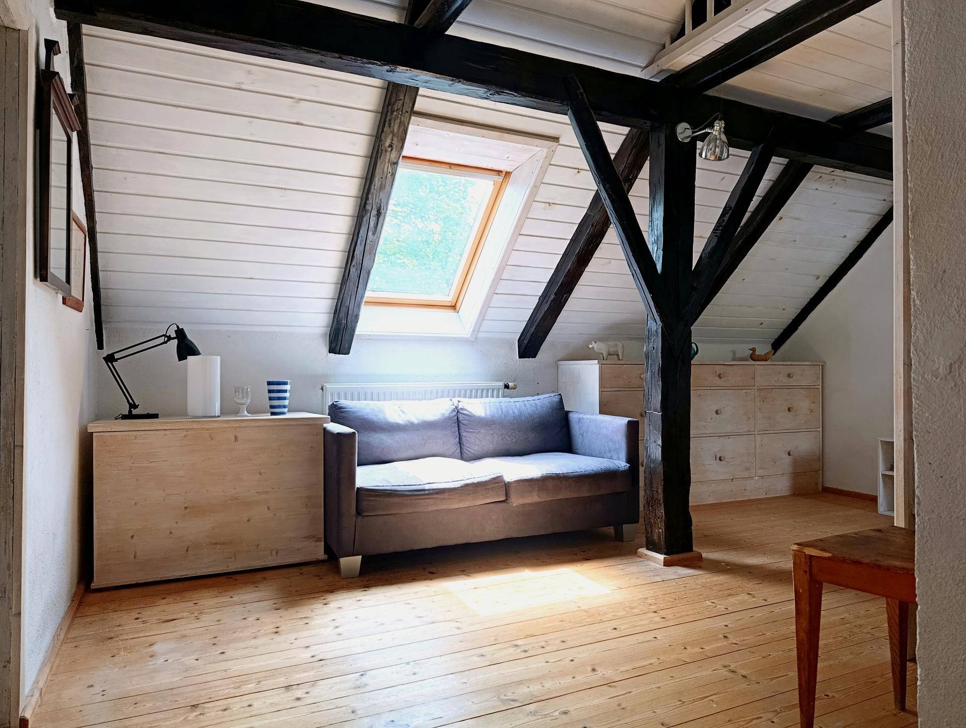 Gemütlicher Wohnbereich im Dachgeschoss mit Sofa, Holzboden und Dachfenster für viel Licht.