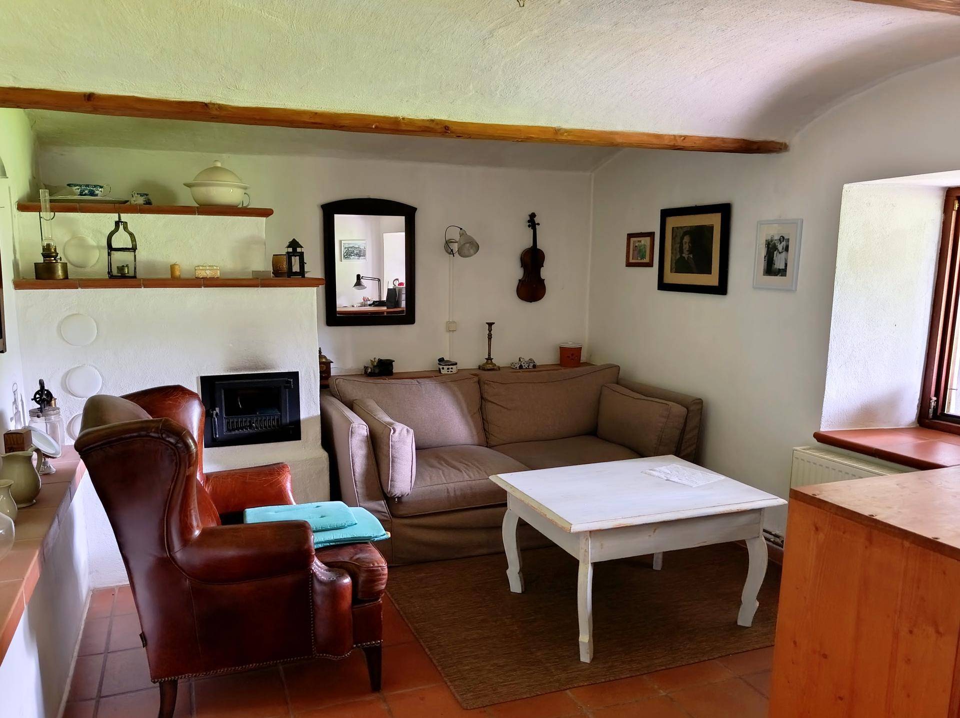 Rustikales Wohnzimmer mit Kamin, bequemen Möbeln und Terrakottafliesen auf dem Boden.