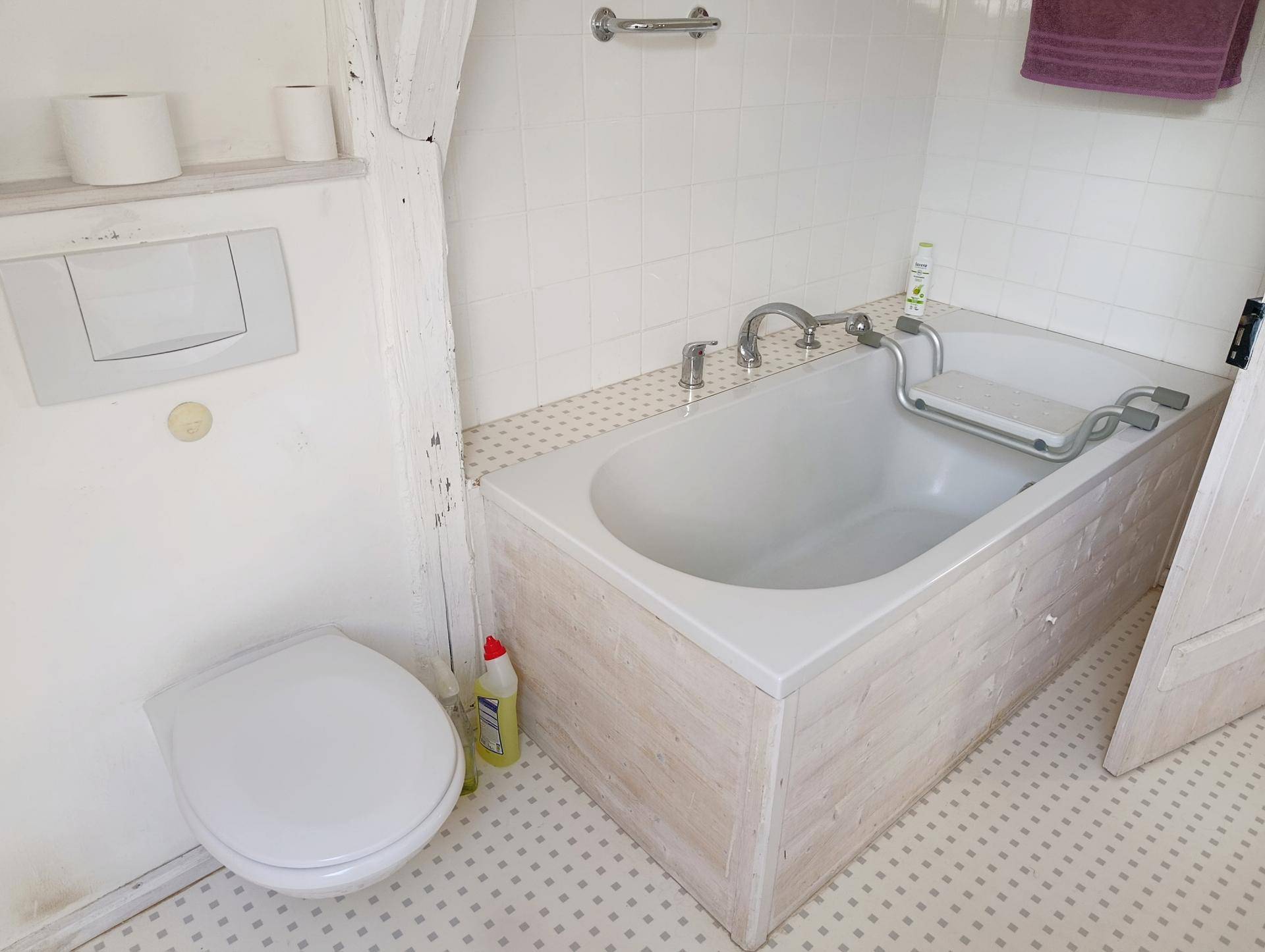 Helles Badezimmer mit Badewanne, Toilette und weißen Fliesen an Wänden und Boden.