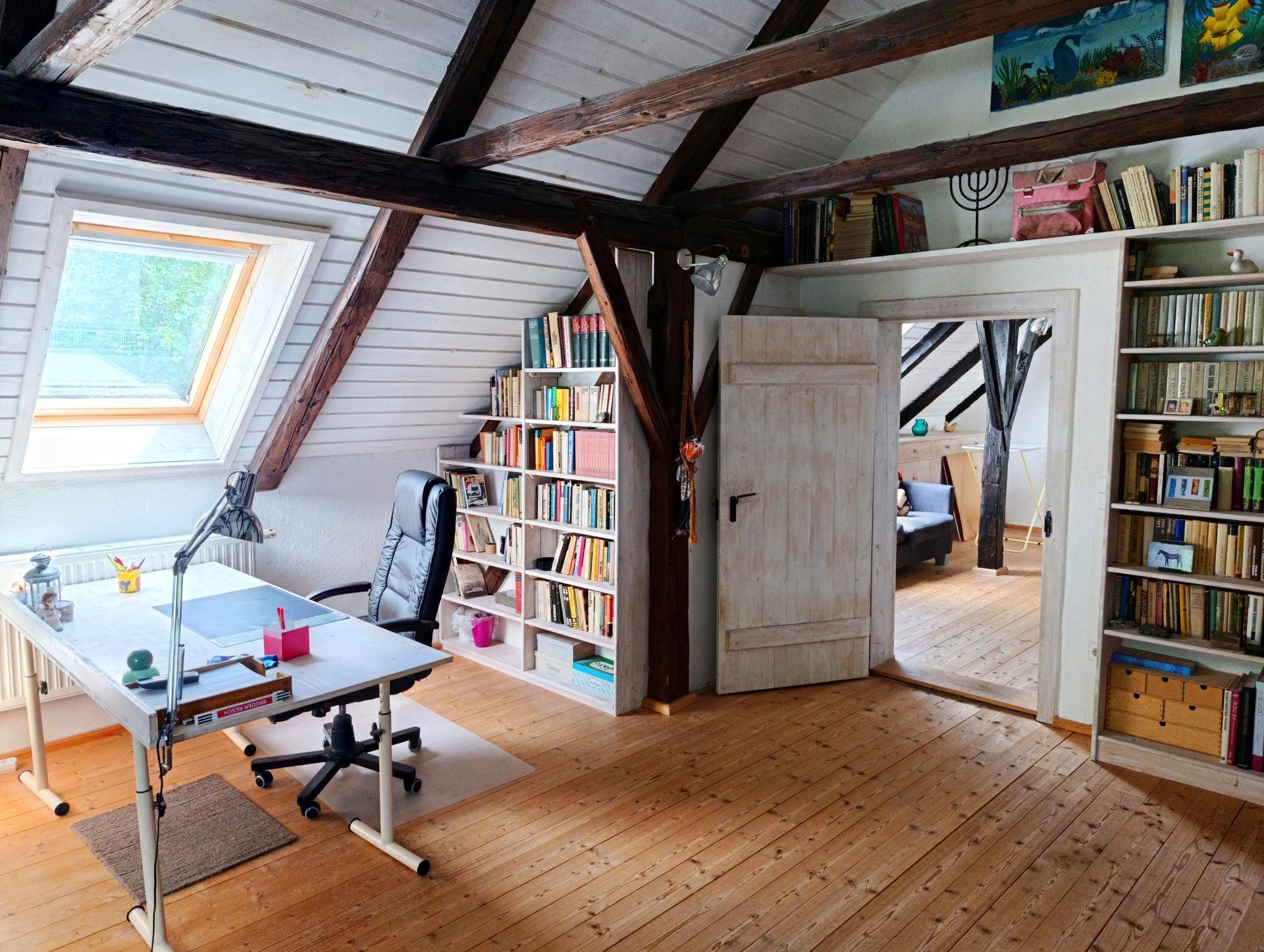 Heller Arbeitsbereich im Dachgeschoss mit Bücherregalen, Holzboden und Dachfenster.