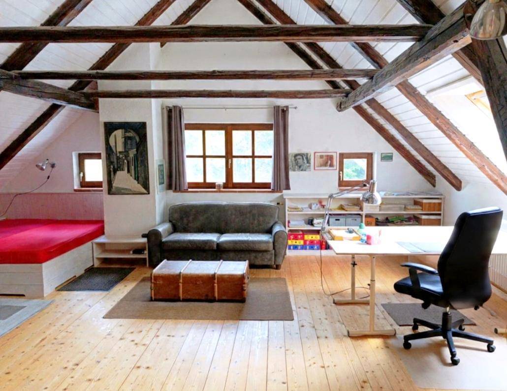 Gemütlicher Wohn- und Arbeitsbereich im Dachgeschoss mit sichtbaren Holzbalken und Holzboden.