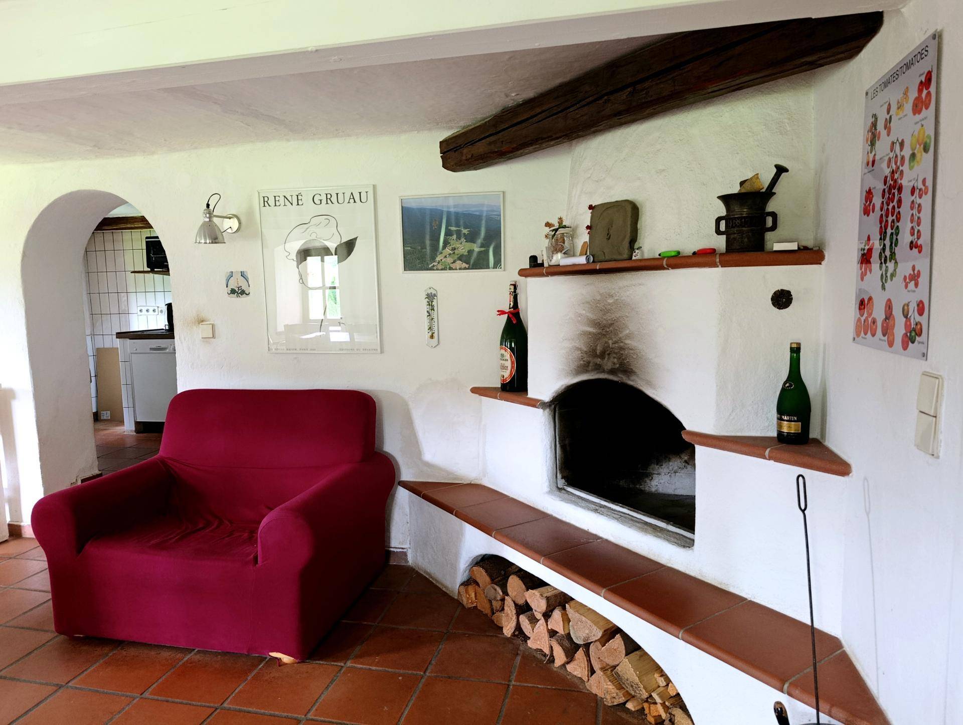 Wohnzimmer mit rustikalem Kamin, Holzscheitlager und einem bequemen roten Sessel.