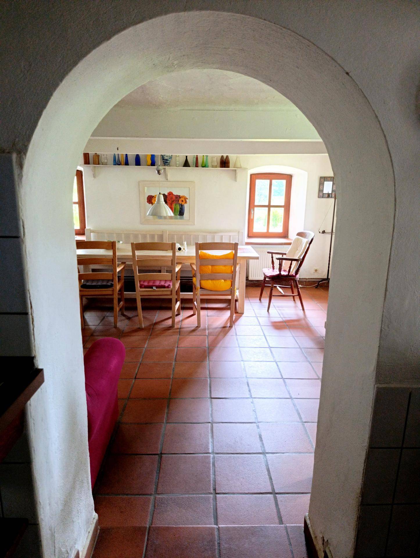 Gewölbter Durchgang führt zu einem hellen Essbereich mit Holztisch und Fenstern.