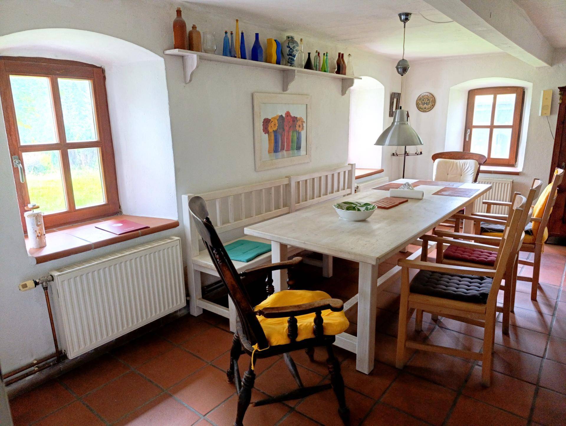 Heller Essbereich mit großem Holztisch, Sitzbank und traditionellen Holzfenstern.