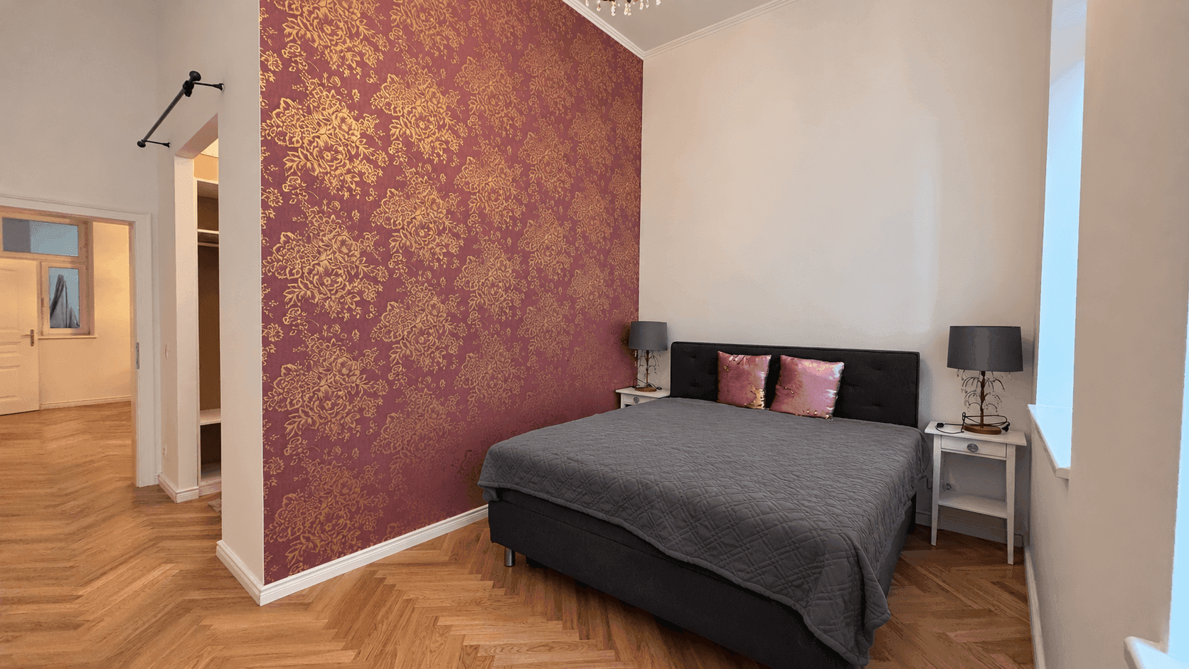 Schlafzimmer mit Doppelbett, Nachttischen und einer auffälligen Tapetenwand, angrenzend an einen begehbaren Kleiderschrank.