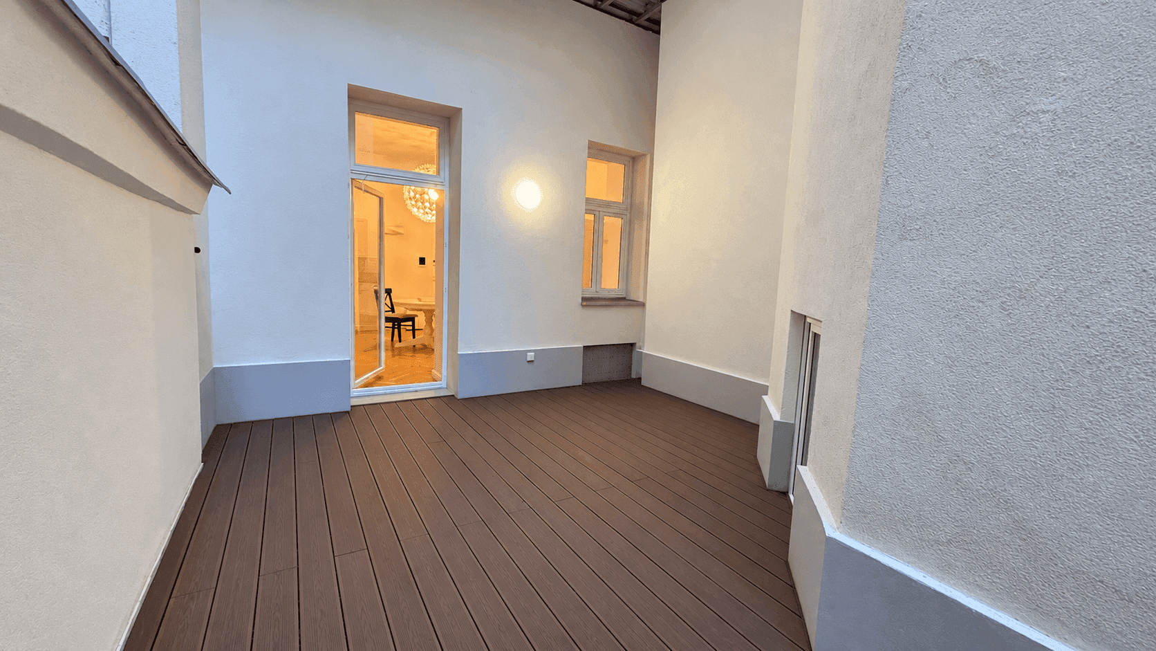 Ruhige Terrasse mit Holzdielenboden und direktem Zugang zu einem hellen Innenraum.