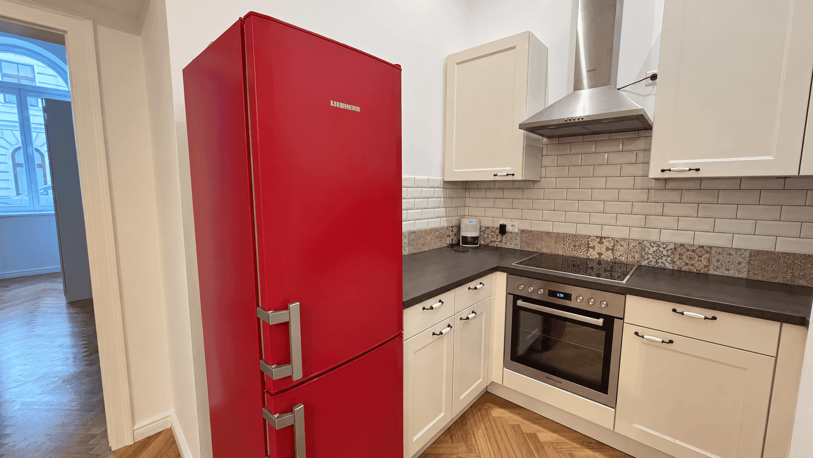 Moderne Küche mit auffälligem rotem Kühlschrank, Induktionskochfeld, Backofen und weißen Schränken.