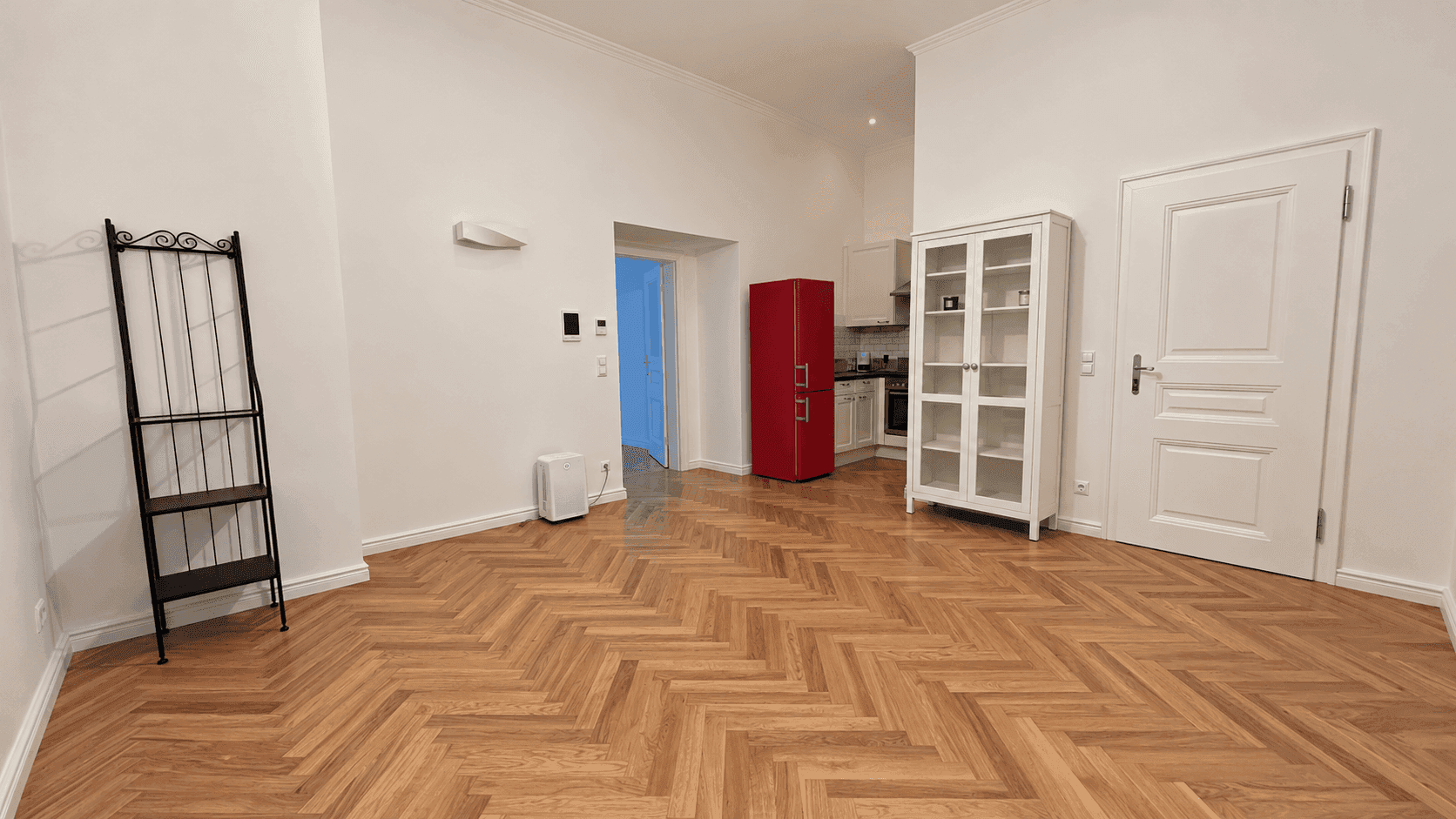Heller Wohnbereich mit Fischgrätparkett, der sich zu einer modernen Küche mit rotem Kühlschrank öffnet.