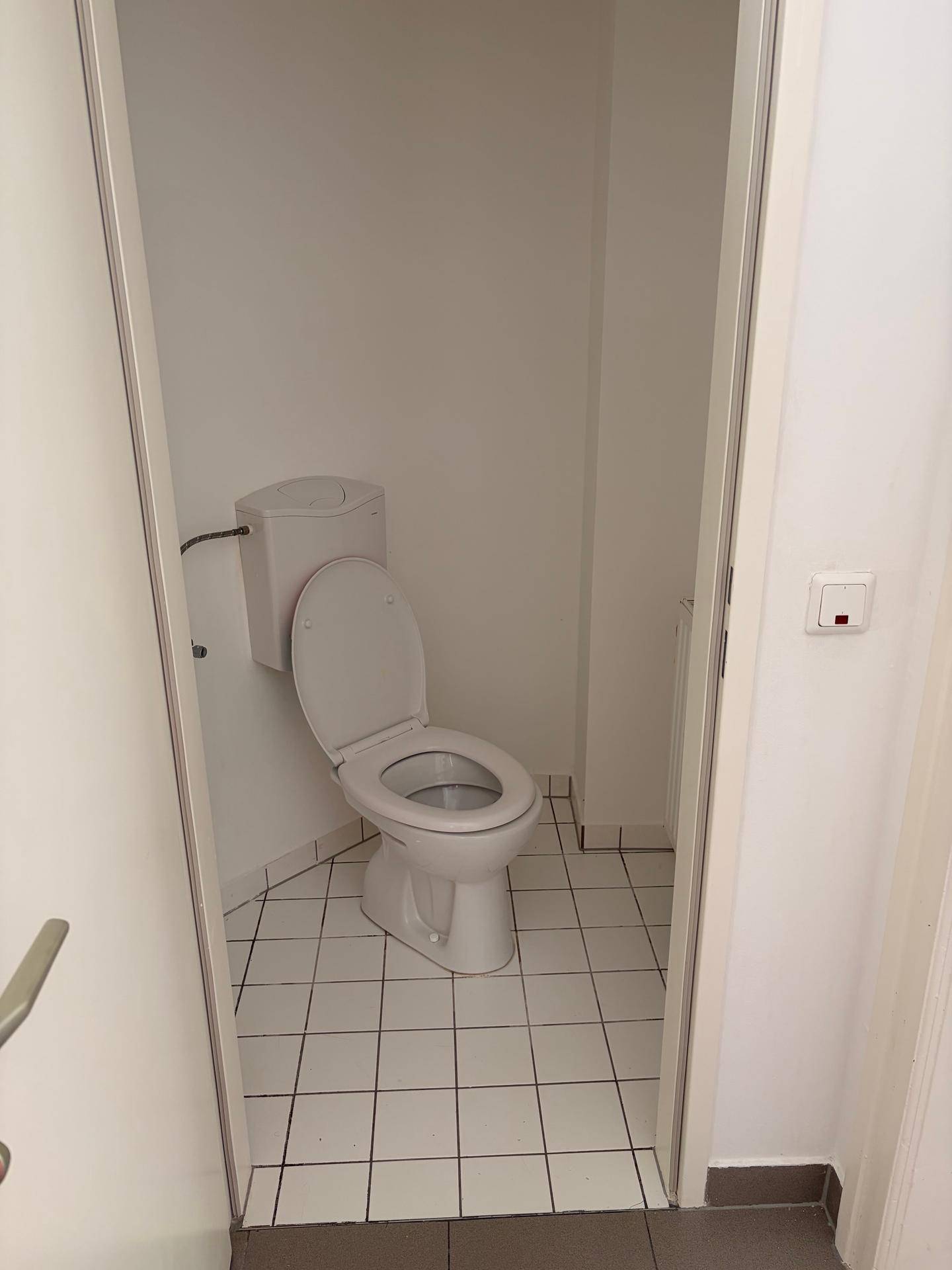 Kleines separates WC mit weißen Fliesen und einfacher Toilette, funktional und sauber gehalten.