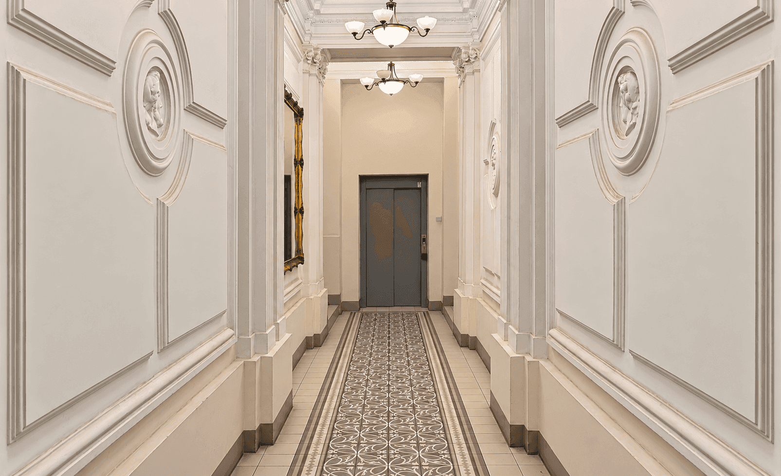 Eleganter Flur in einem Altbau mit Stuckverzierungen, dekorativem Boden und einem Aufzug am Ende.