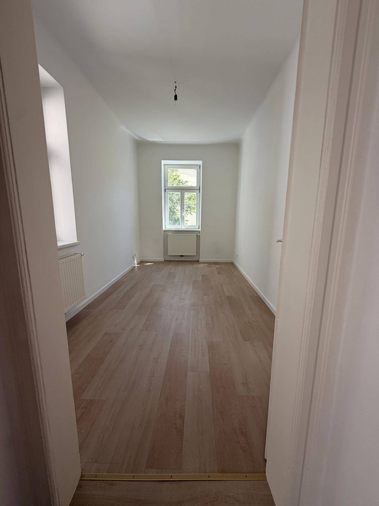 Langer, heller Raum mit Laminatboden und einem Fenster, ideal als Schlafzimmer oder Arbeitszimmer.