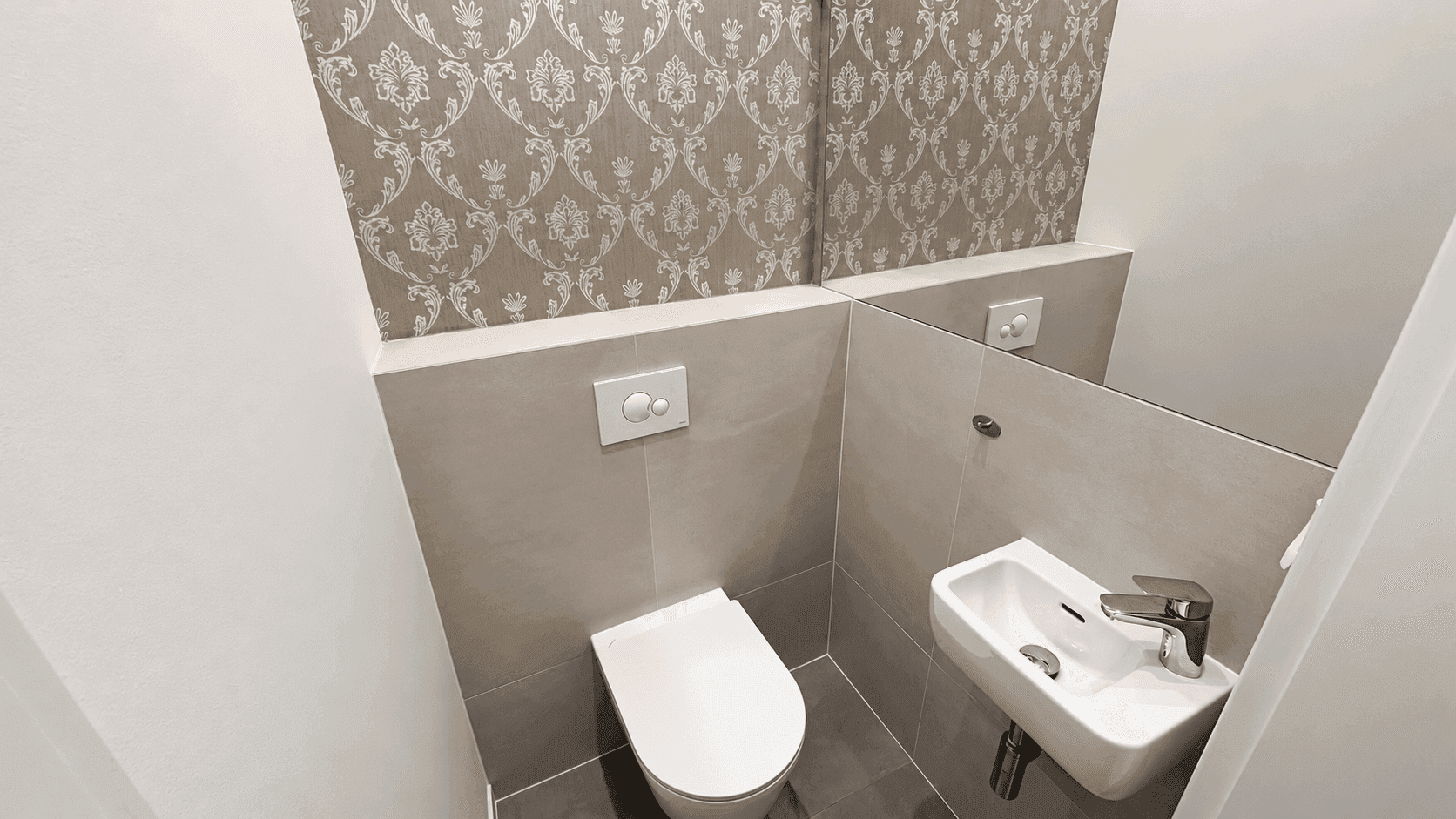 Kleines Gäste-WC mit wandhängender Toilette, kleinem Waschbecken und dekorativer Tapete.