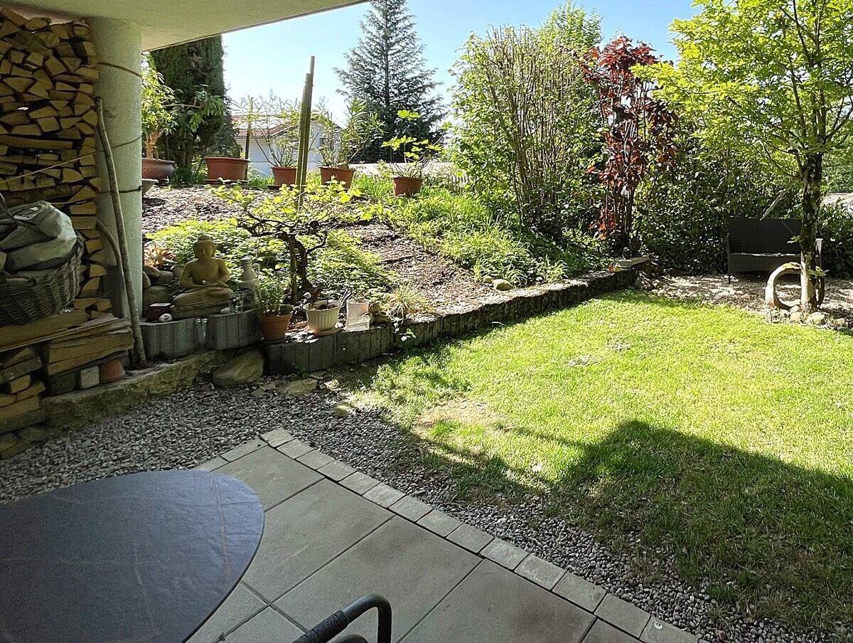 Überdachte Terrasse mit Steinplatten und Blick auf den grünen Gartenbereich mit Holzstapel.