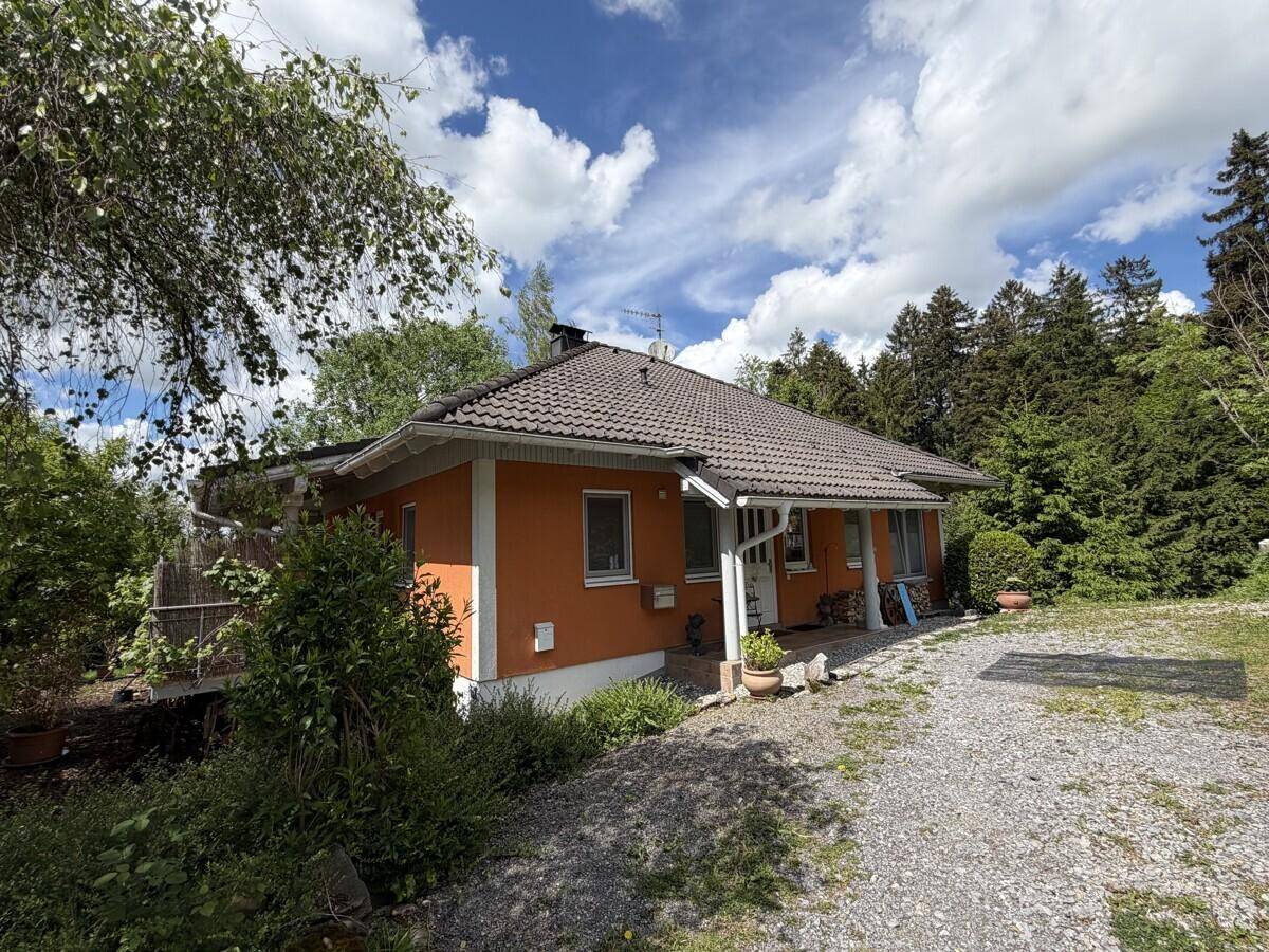 Einfamilienhaus mit orangefarbener Fassade, Satteldach und Schotterauffahrt umgeben von Bäumen.