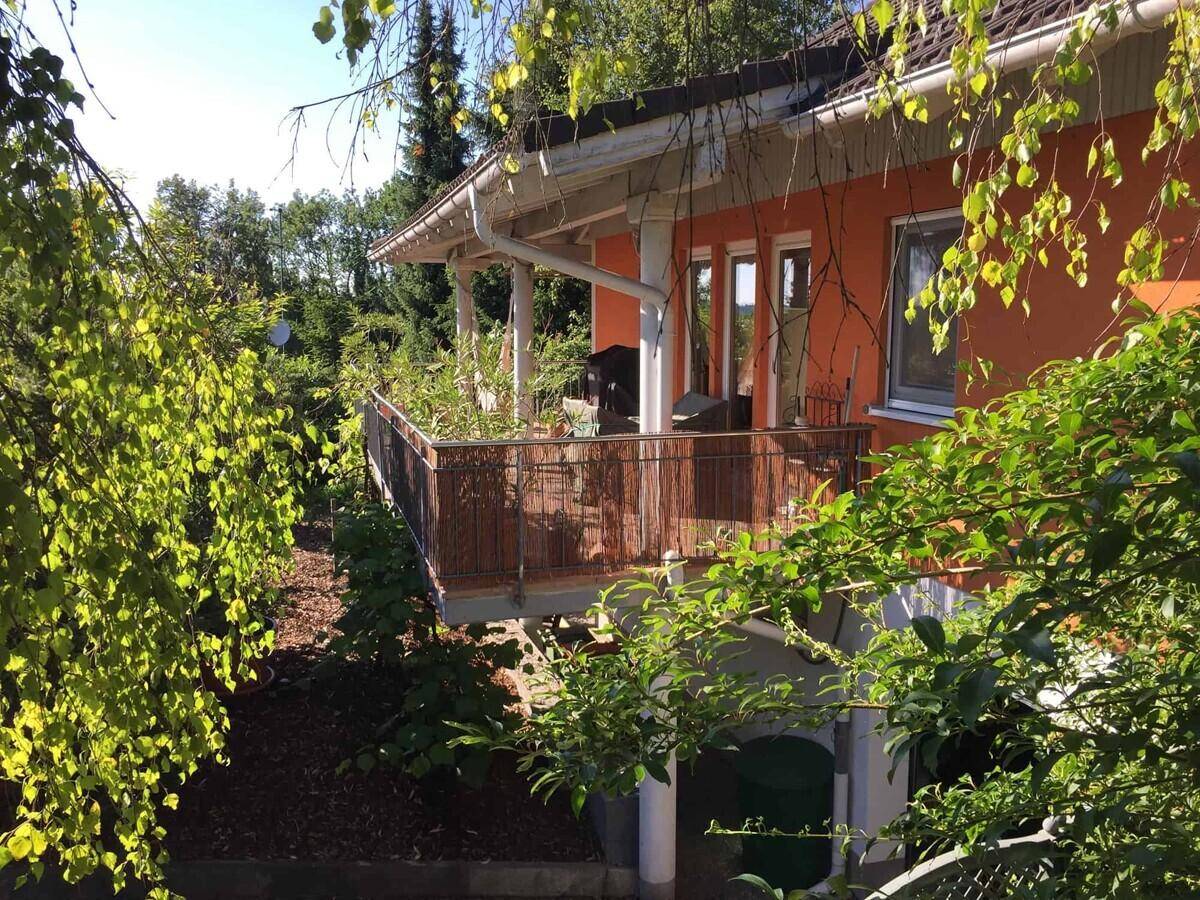 Balkon mit Holzgeländer und Blick auf die grüne Umgebung, umgeben von Bäumen und Sträuchern.