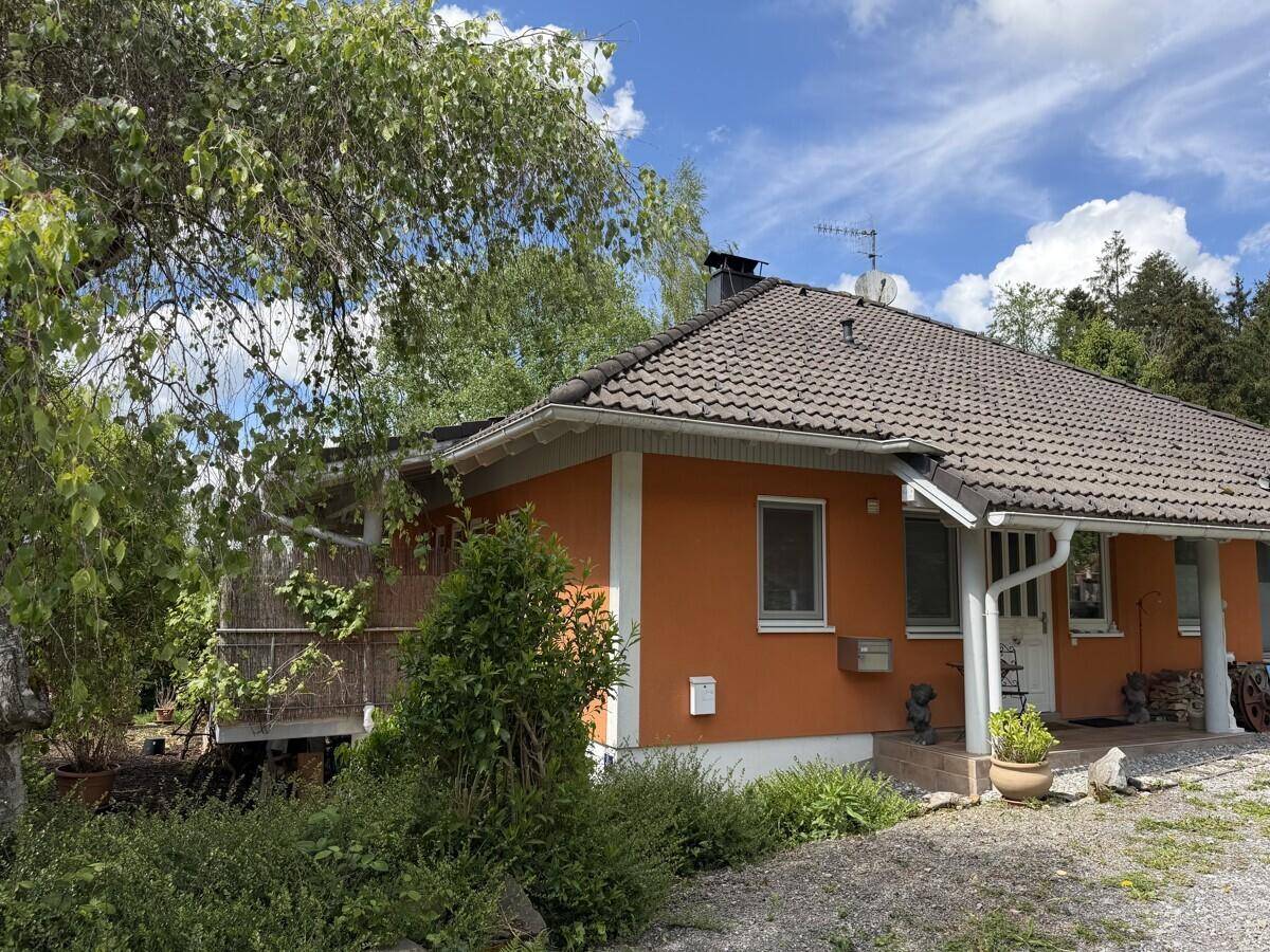 Haus mit orangefarbener Fassade, überdachtem Eingangsbereich und Schotterauffahrt im Grünen.
