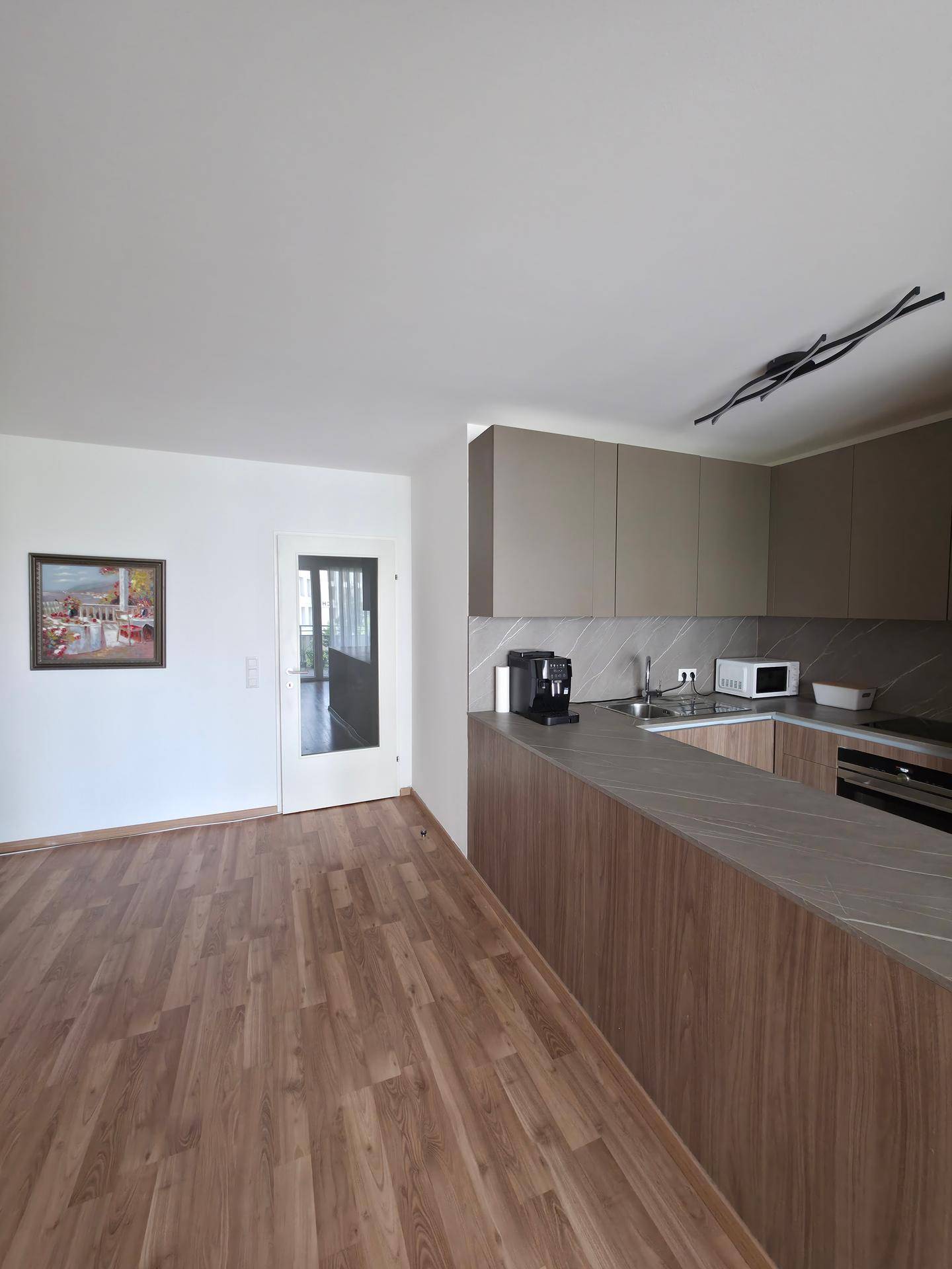 Offene Küche mit Holzfußboden, grauer Arbeitsplatte und Blick in den Wohnbereich.