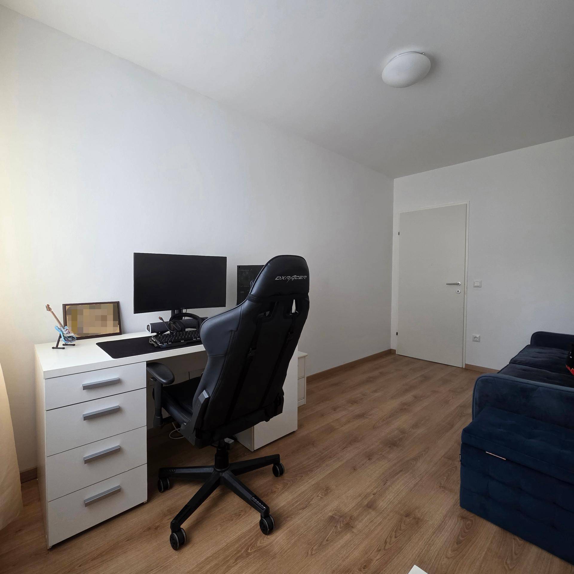 Arbeitsbereich mit Schreibtisch, Gaming-Stuhl und Computer in einem hellen Zimmer.