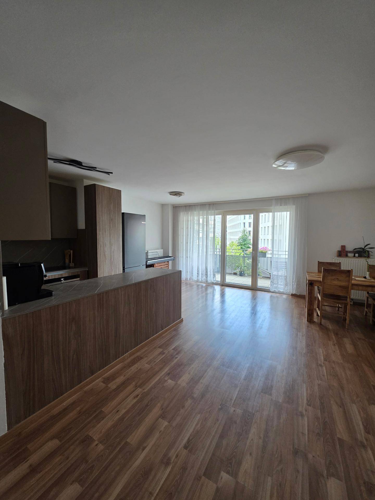 Heller Wohn-Essbereich mit offener Küche, Holzfußboden und Zugang zum Balkon.