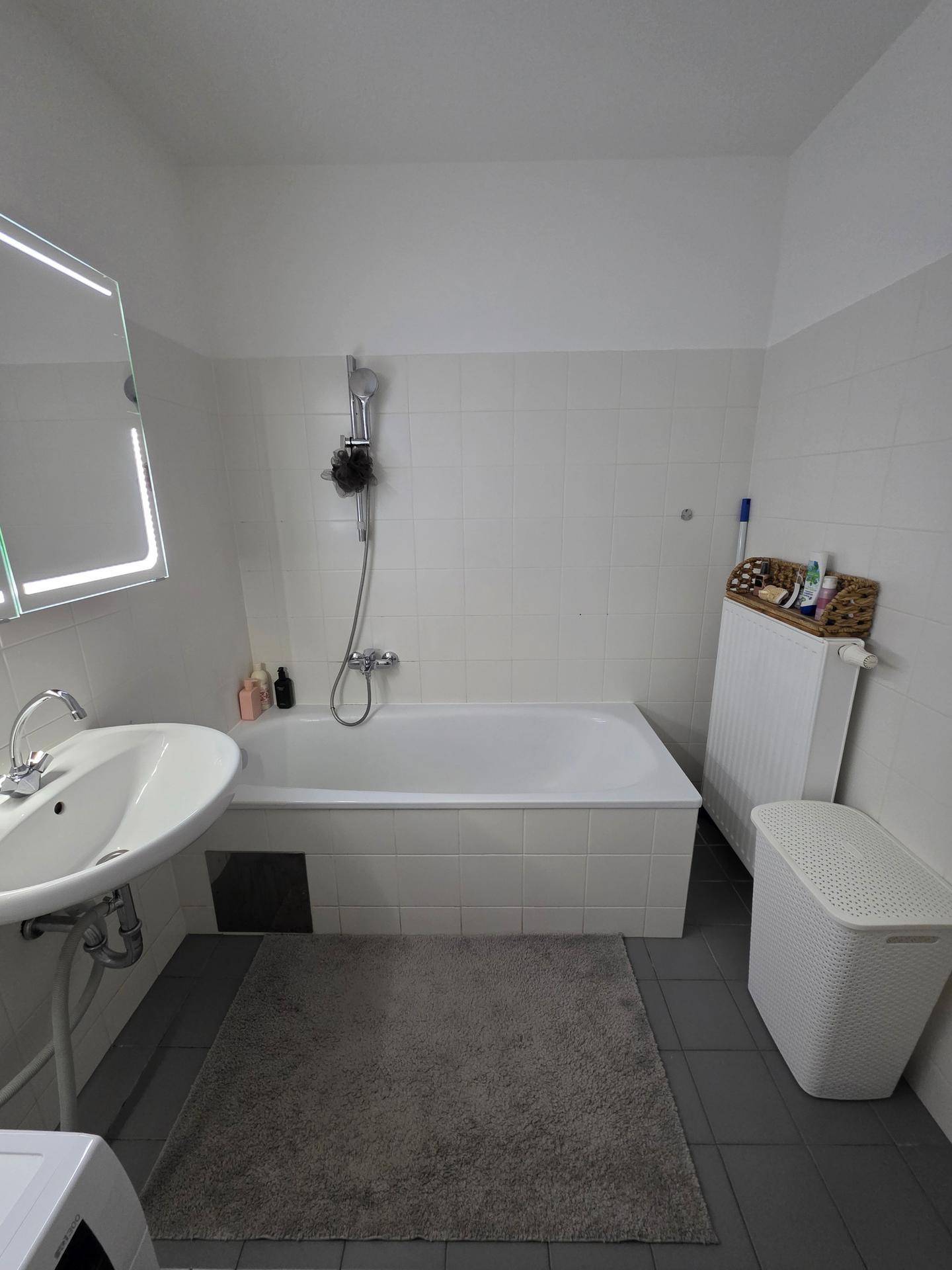Helles Badezimmer mit Badewanne, Waschbecken und Fliesen an Wänden und Boden.
