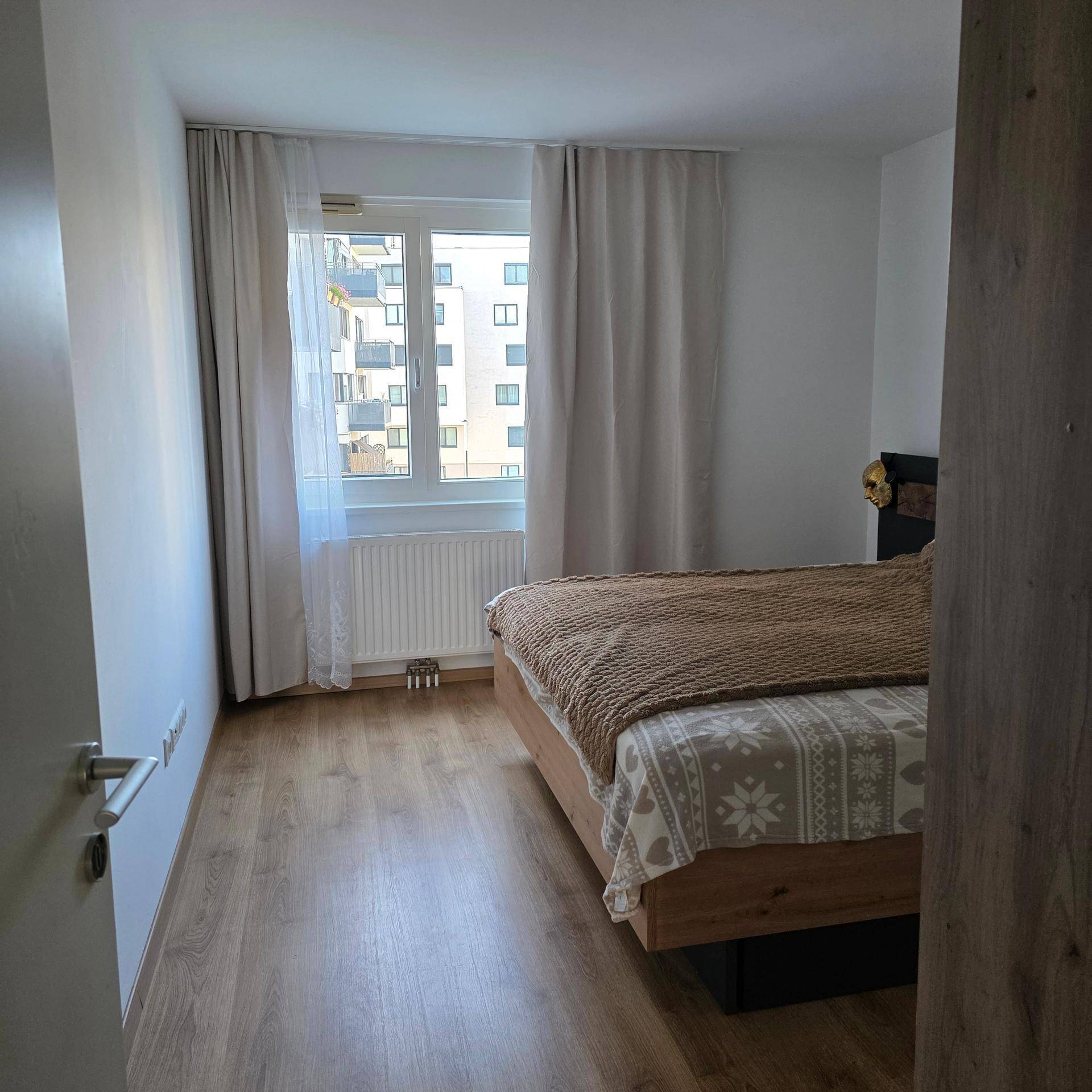 Schlafzimmer mit Holzfußboden, Doppelbett und Fenster mit Blick auf die Umgebung.