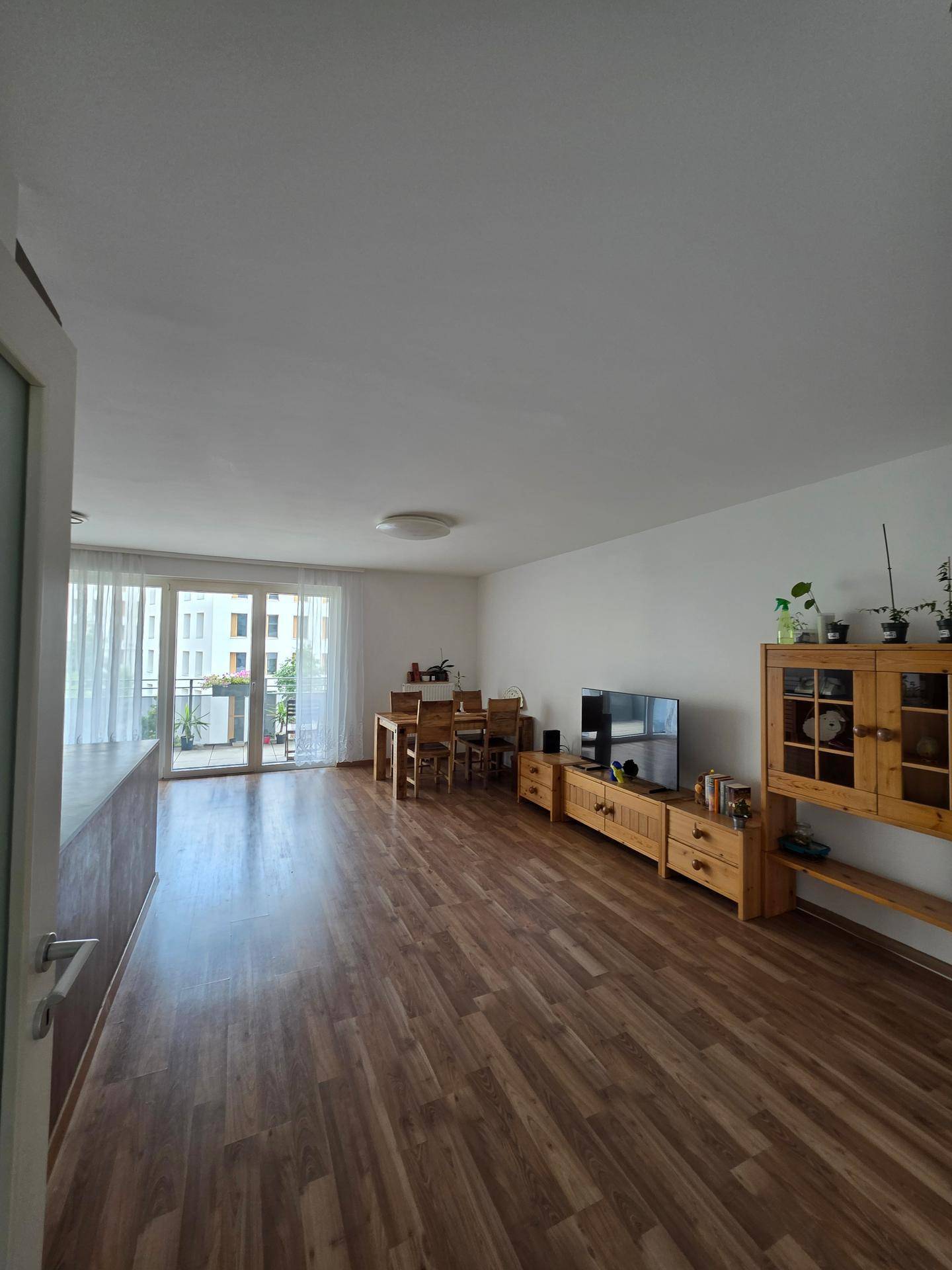 Geräumiger Wohn-Essbereich mit Holzfußboden, Esstisch und Zugang zum Balkon.