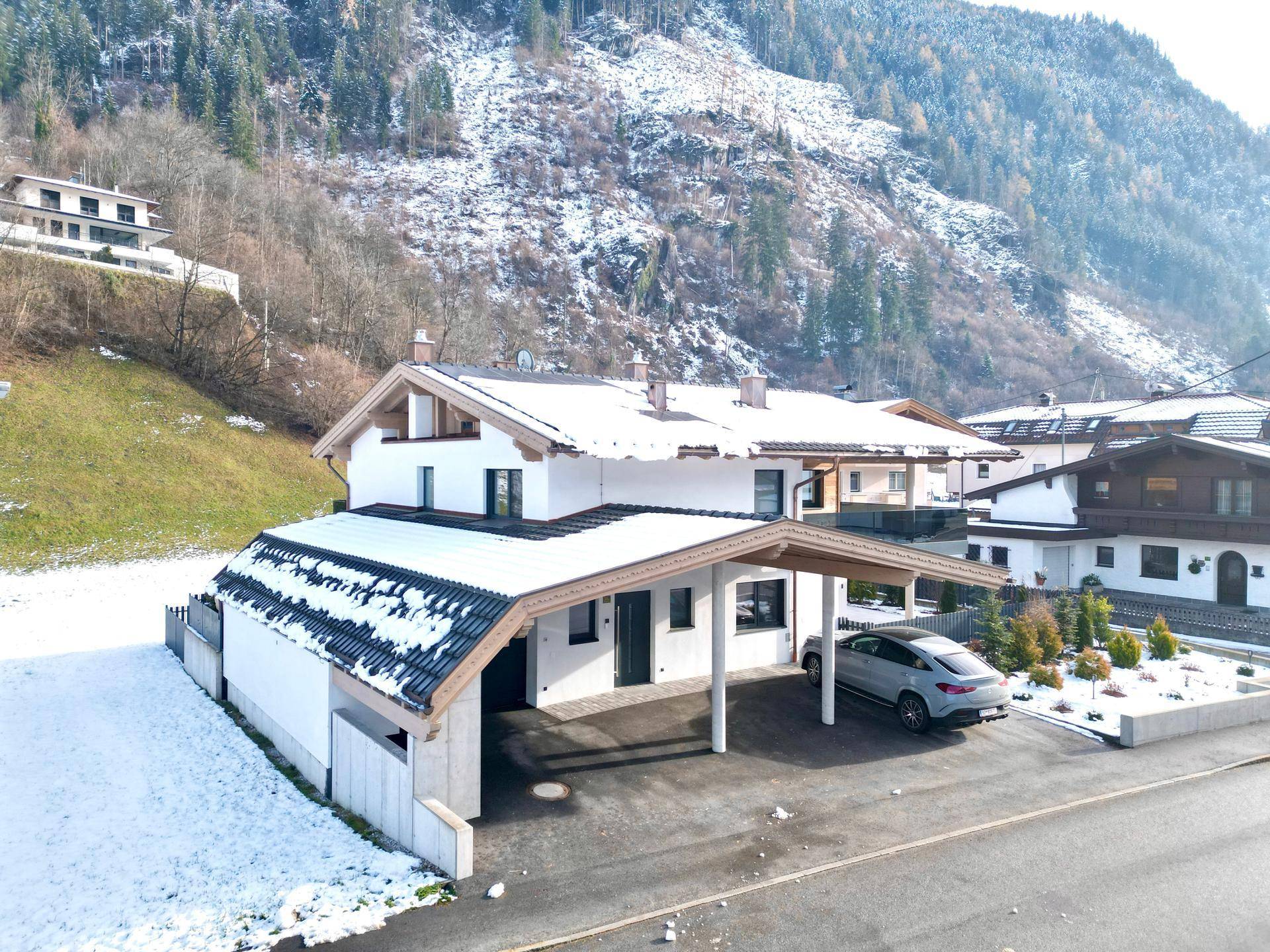 Modernes Haus mit Carport und gepflegtem Vorgarten in einer verschneiten Hanglage.
