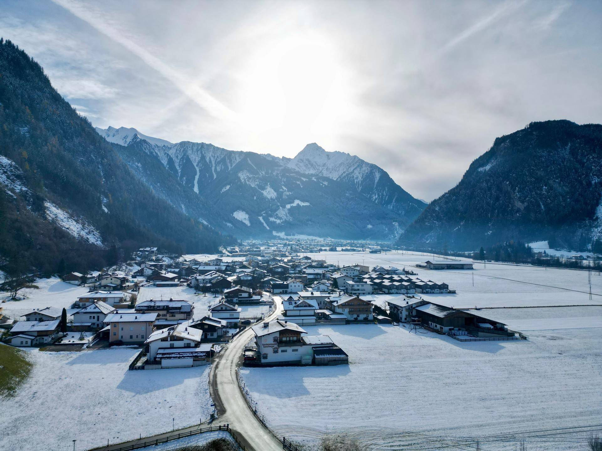 Weitläufige Luftaufnahme eines verschneiten Dorfes in einem Tal, umgeben von majestätischen Bergen.
