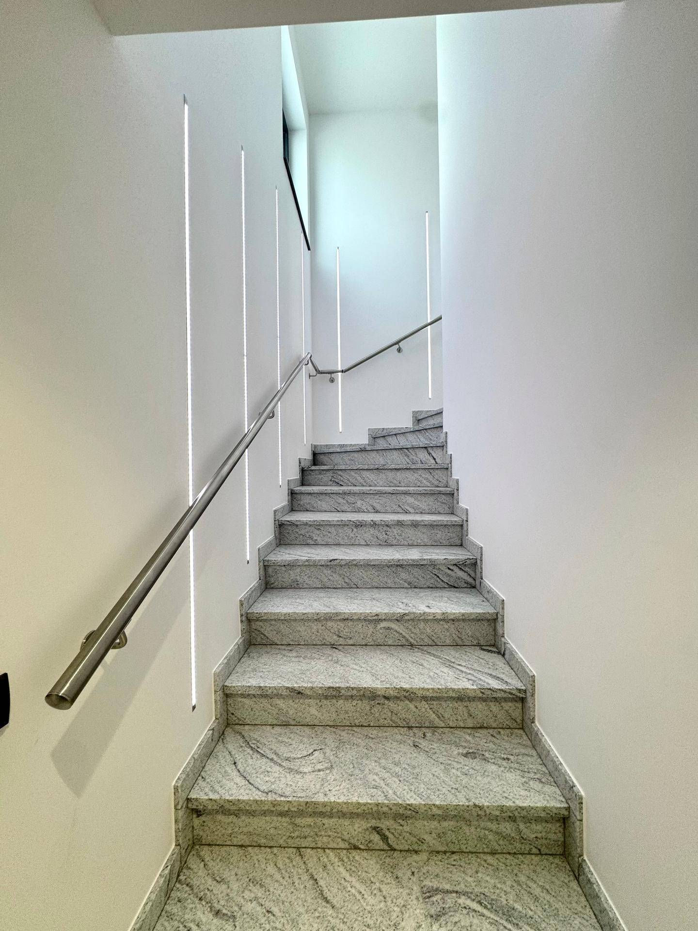 Elegantes Treppenhaus mit Marmorstufen und modernem Geländer, beleuchtet durch integrierte LED-Streifen.
