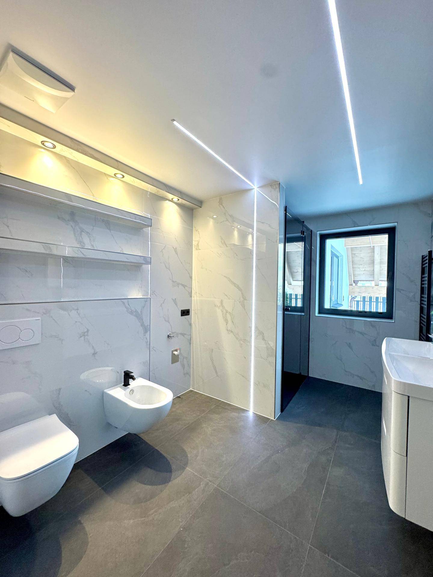 Luxuriöses Badezimmer mit Bidet, Wand-WC, modernem Waschtisch und eleganten Marmorfliesen.