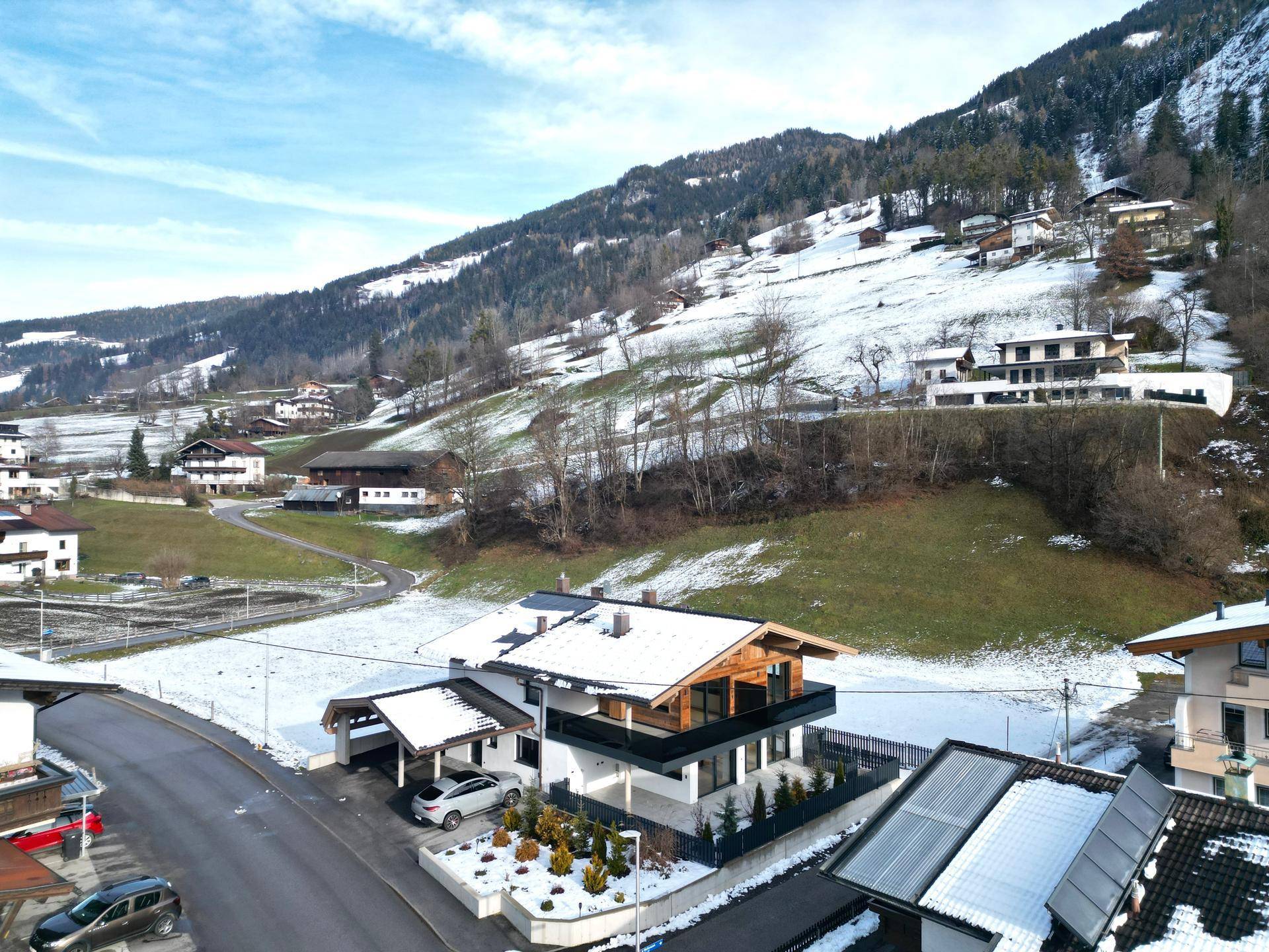 Vogelperspektive eines modernen Hauses mit Balkon und umliegender verschneiter Hügellandschaft.