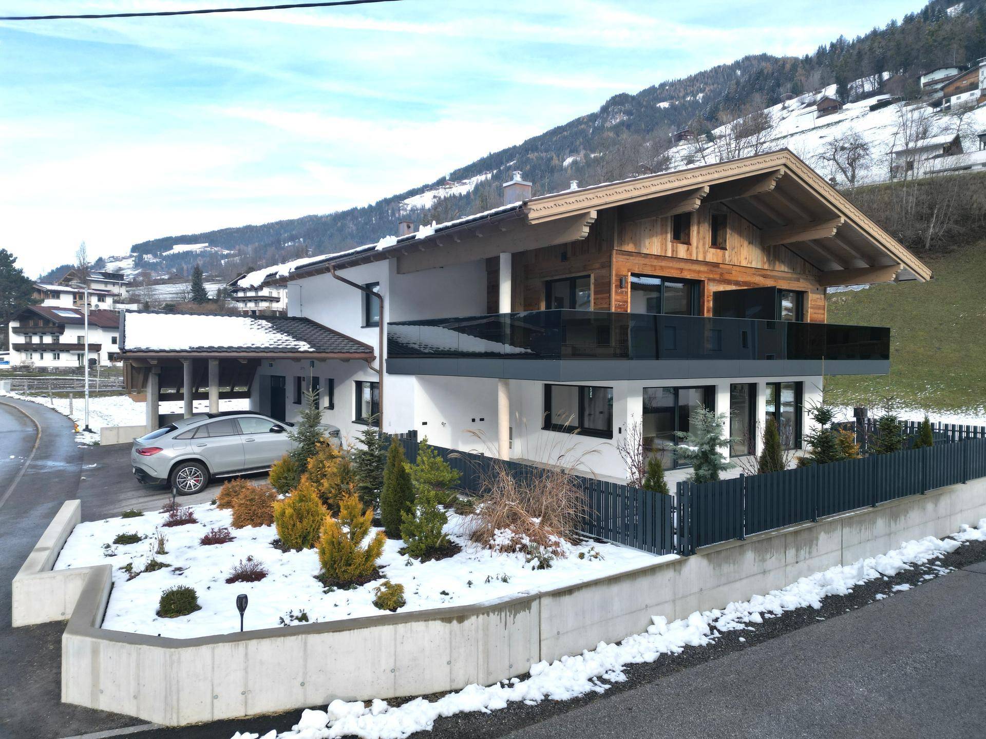 Elegantes modernes Haus mit weißer Fassade, Holzverkleidung und großem Balkon mit Glasgeländer.