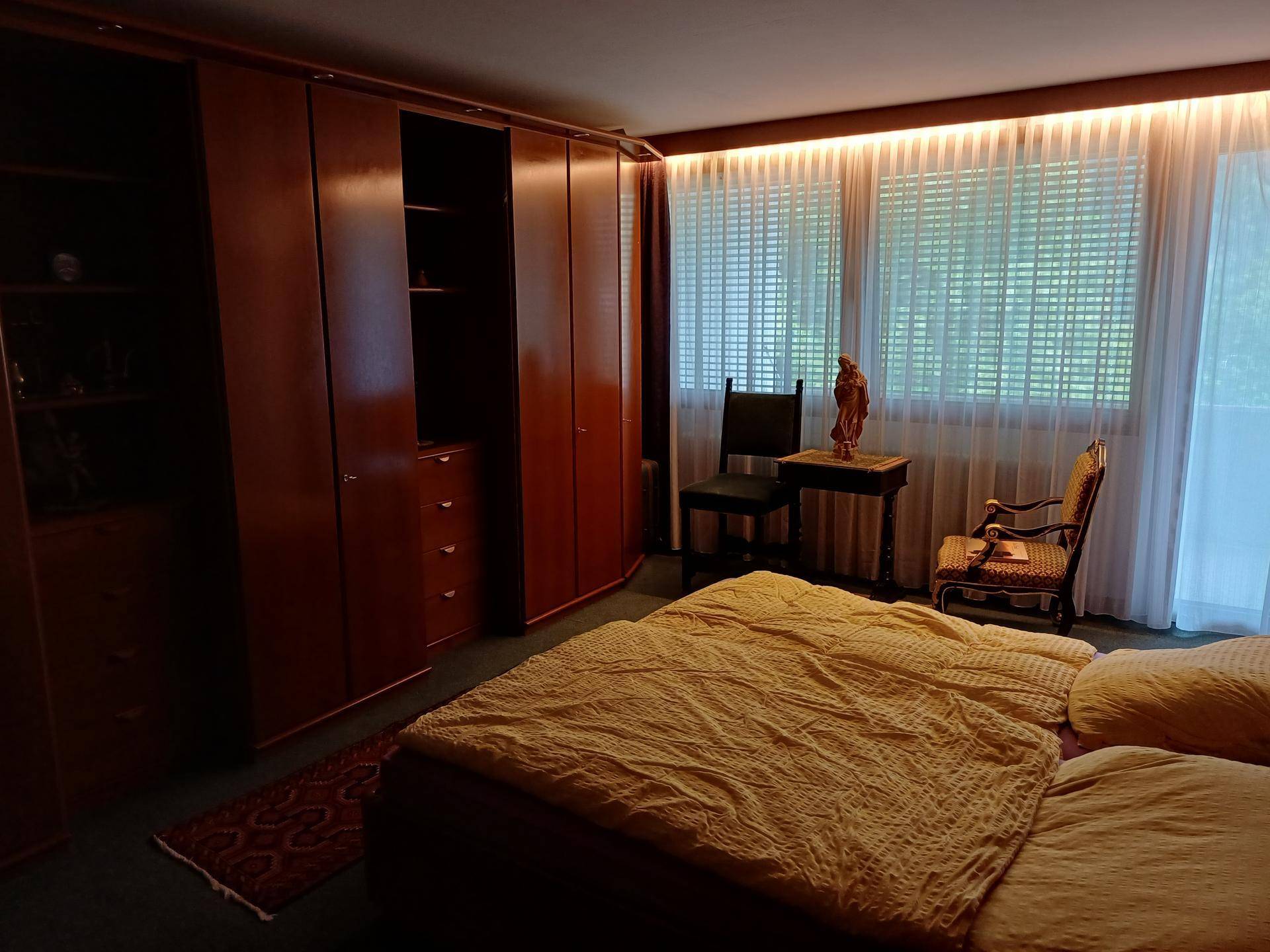 Schlafzimmer mit Doppelbett, Einbauschränken und großen Fenstern mit Vorhängen.