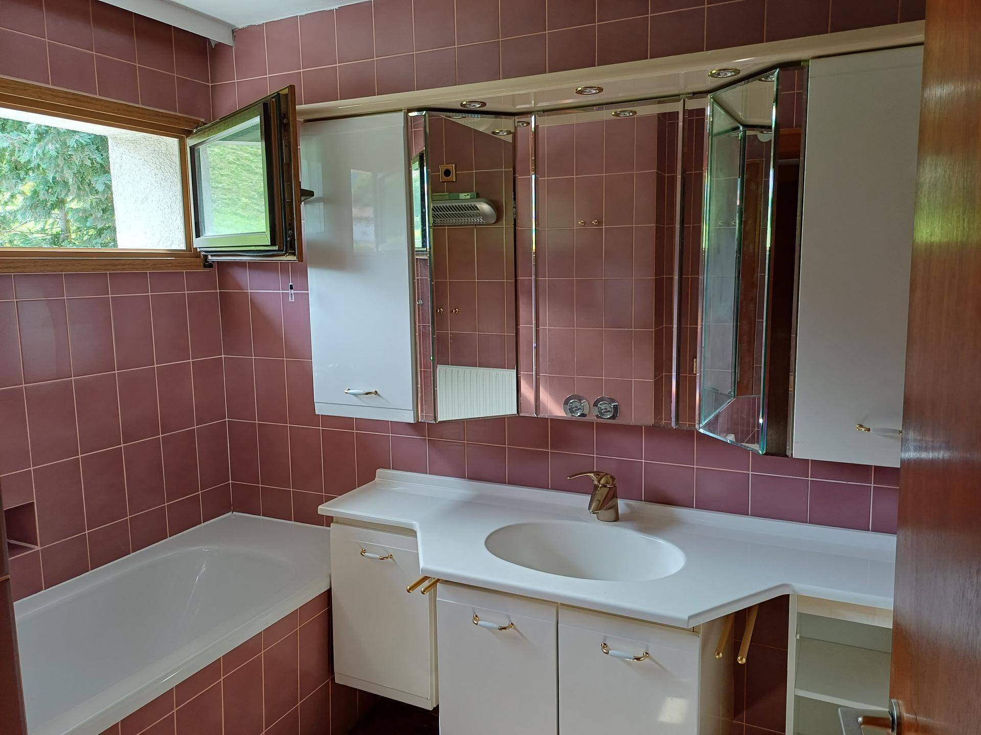 Badezimmer mit Badewanne, Waschbecken, Spiegelschrank und rosafarbenen Fliesen.