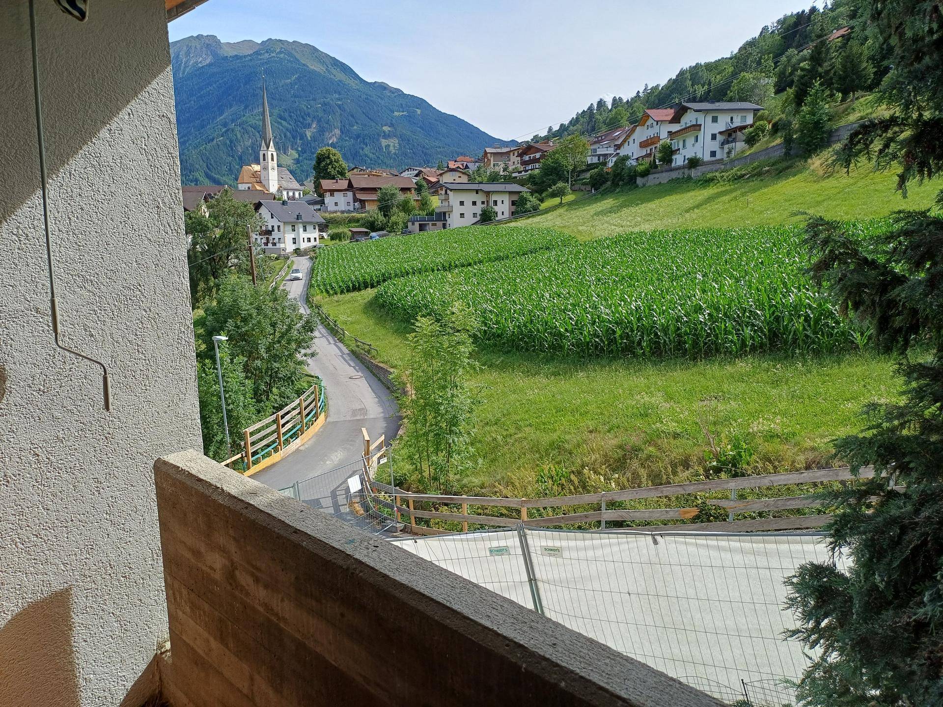 Balkon mit weitem Blick auf eine ländliche Landschaft, Berge und ein Dorf mit Kirche.