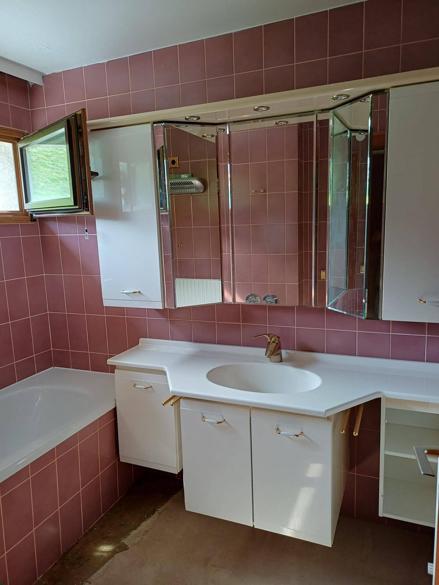 Badezimmer mit Badewanne, Waschbecken, Spiegelschrank und rosafarbenen Fliesen.