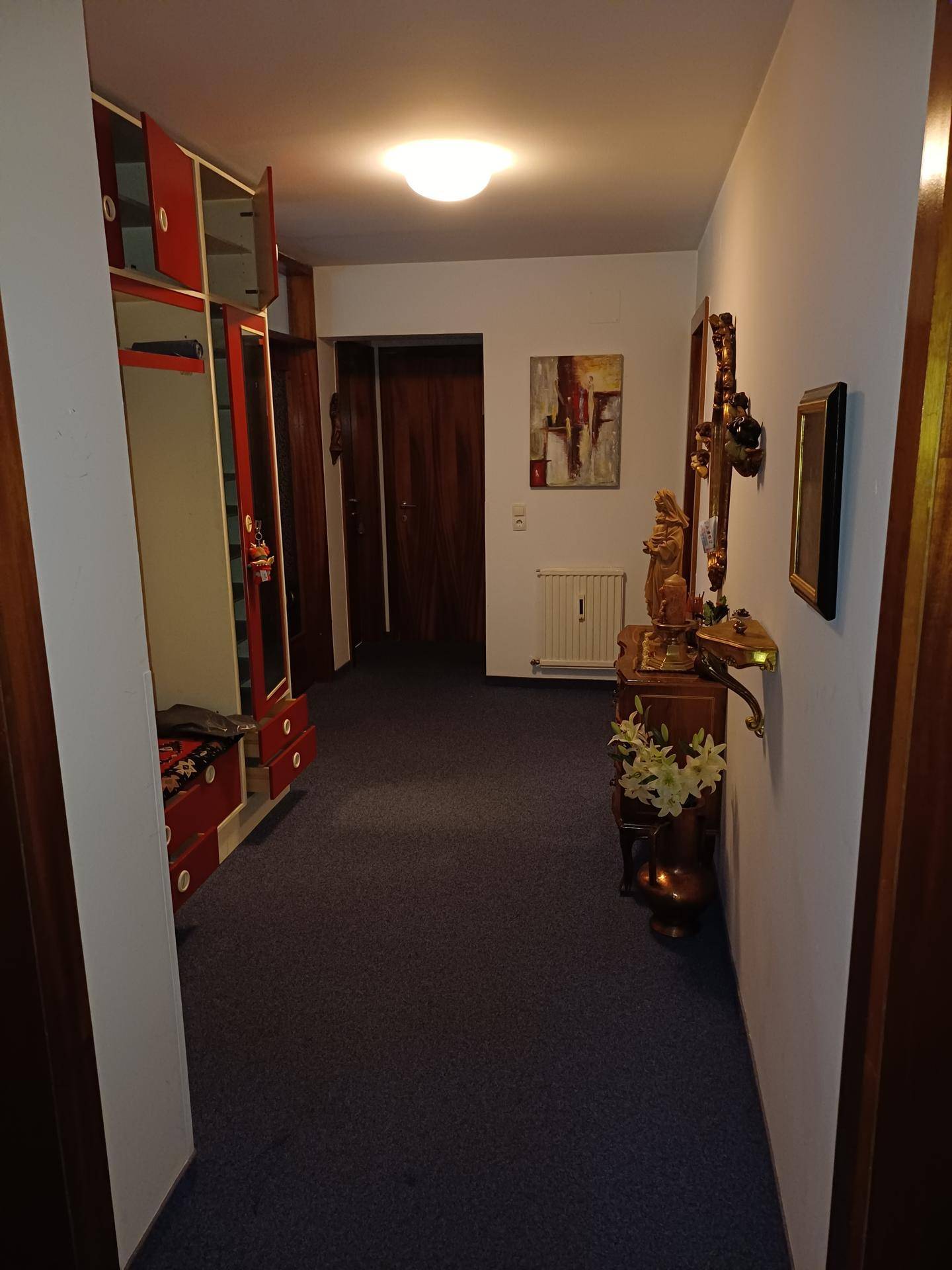 Langer Flur mit Teppichboden, Holzvertäfelung und einem dekorativen Konsolentisch.