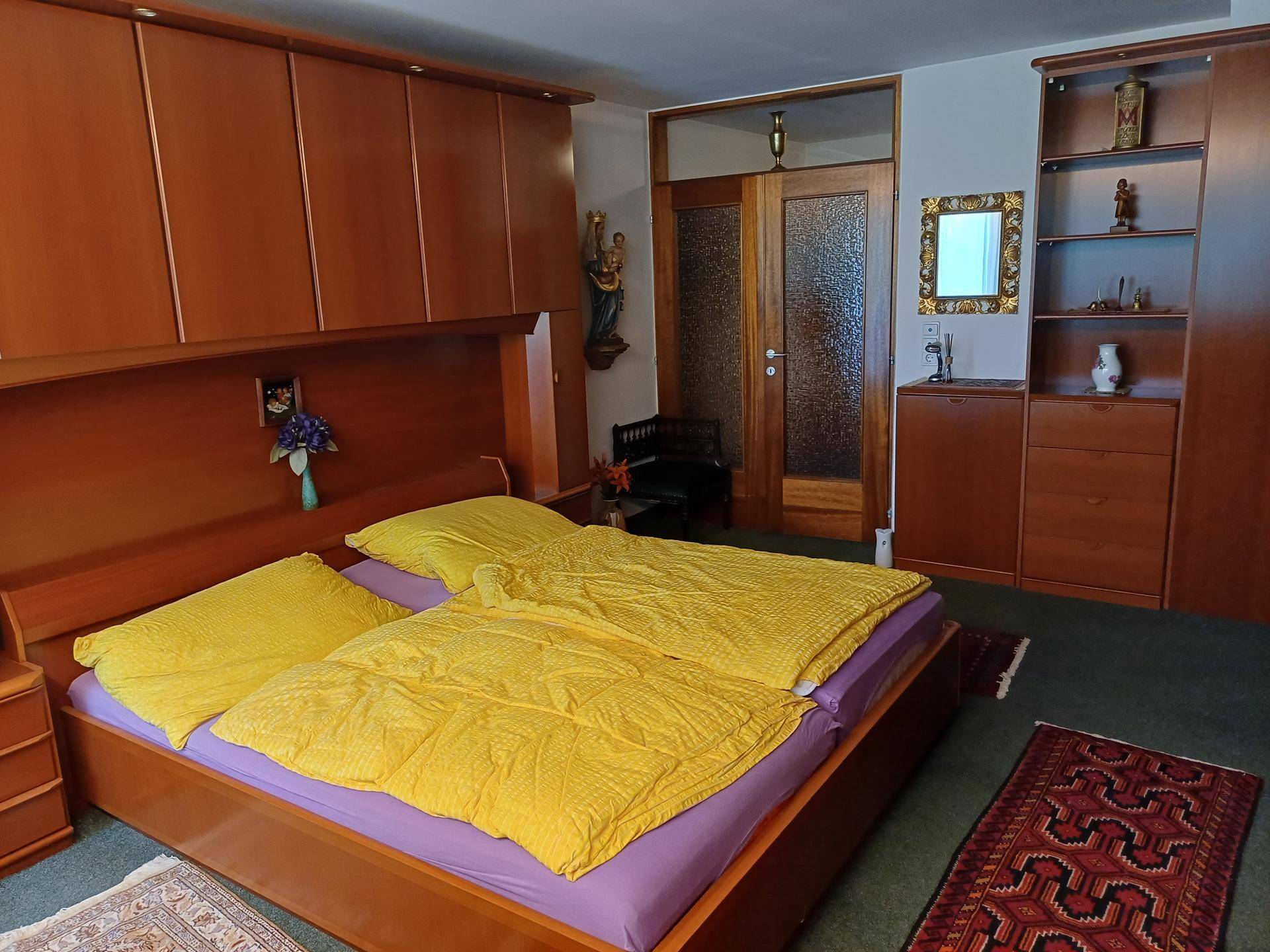 Schlafzimmer mit Doppelbett, Holzschränken und einem Spiegel, der den Raum größer wirken lässt.