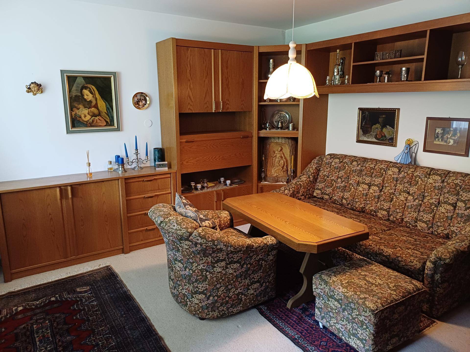 Gemütliches Wohnzimmer mit Holzmöbeln, floral gemustertem Sofa und Teppichboden.