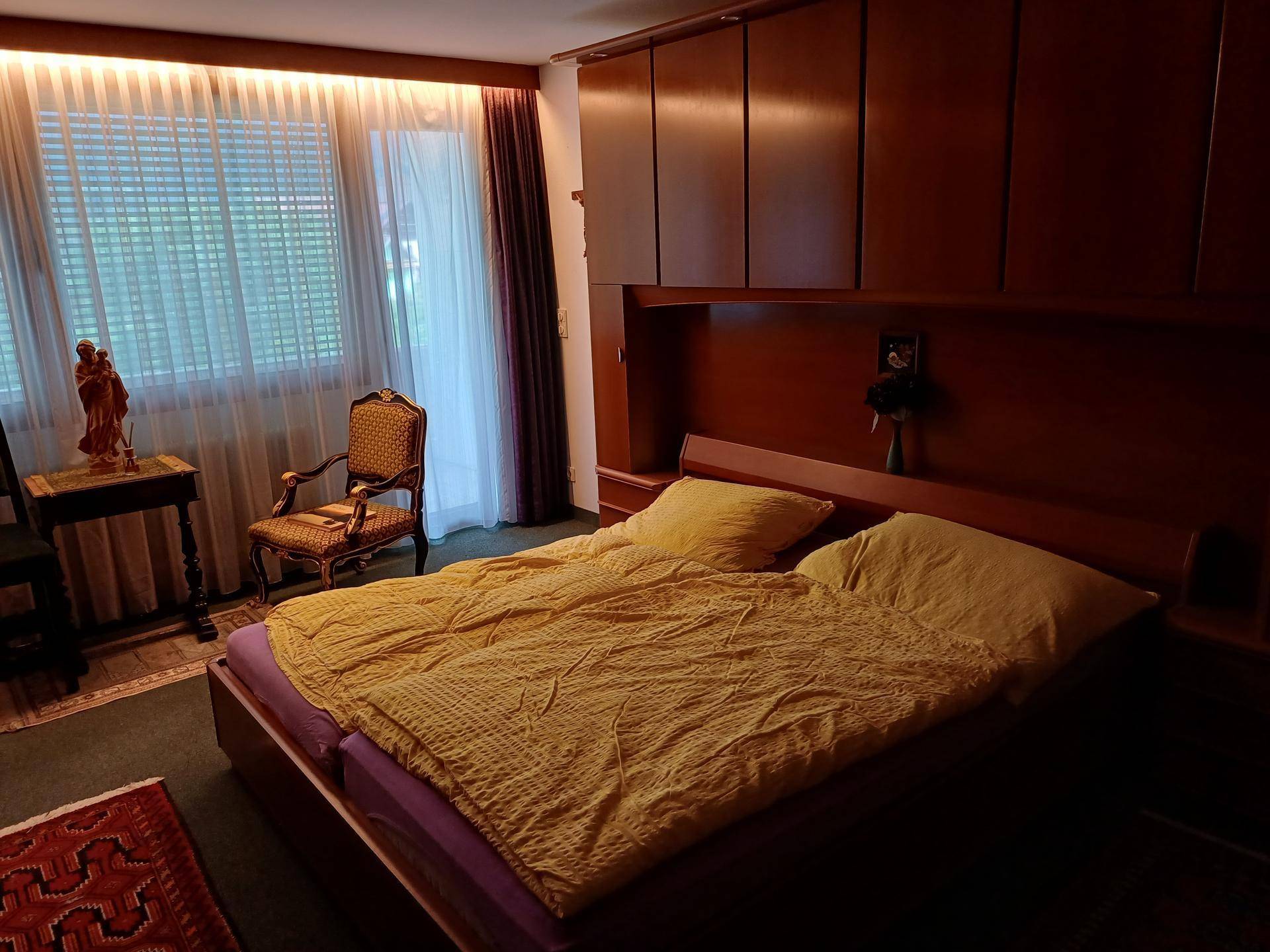Gemütliches Schlafzimmer mit Doppelbett, Holzmöbeln und indirekter Beleuchtung über den Fenstern.