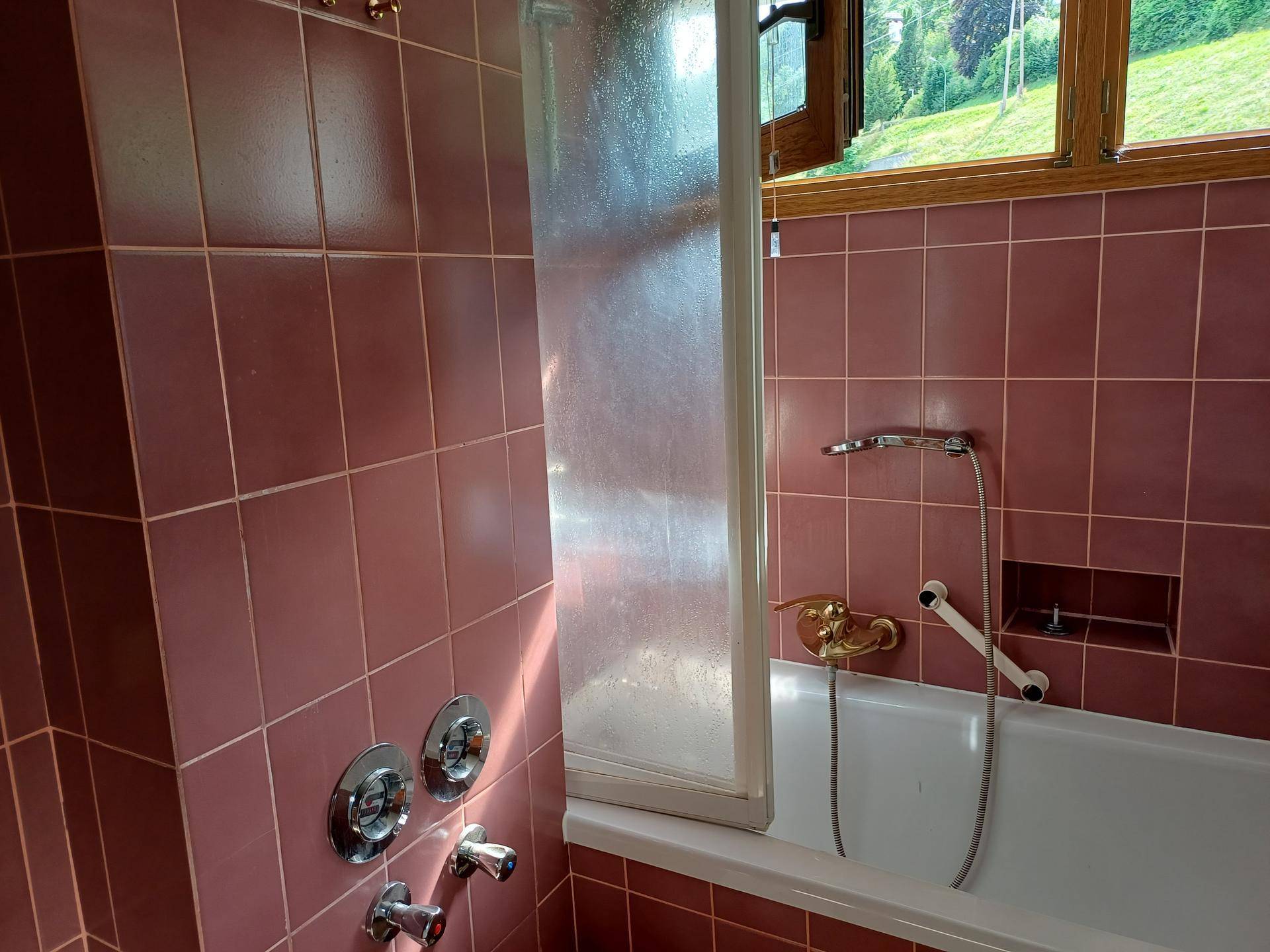 Badezimmer mit Badewanne, Duschabtrennung und rosafarbenen Fliesen im Retro-Stil.