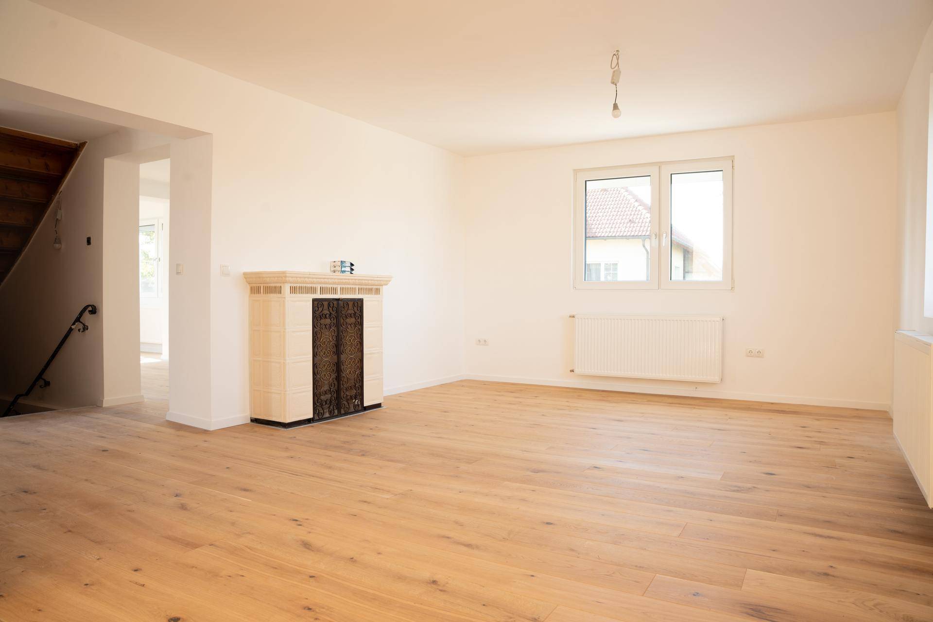 Helles Wohnzimmer mit hellem Holzboden und traditionellem Kachelofen.