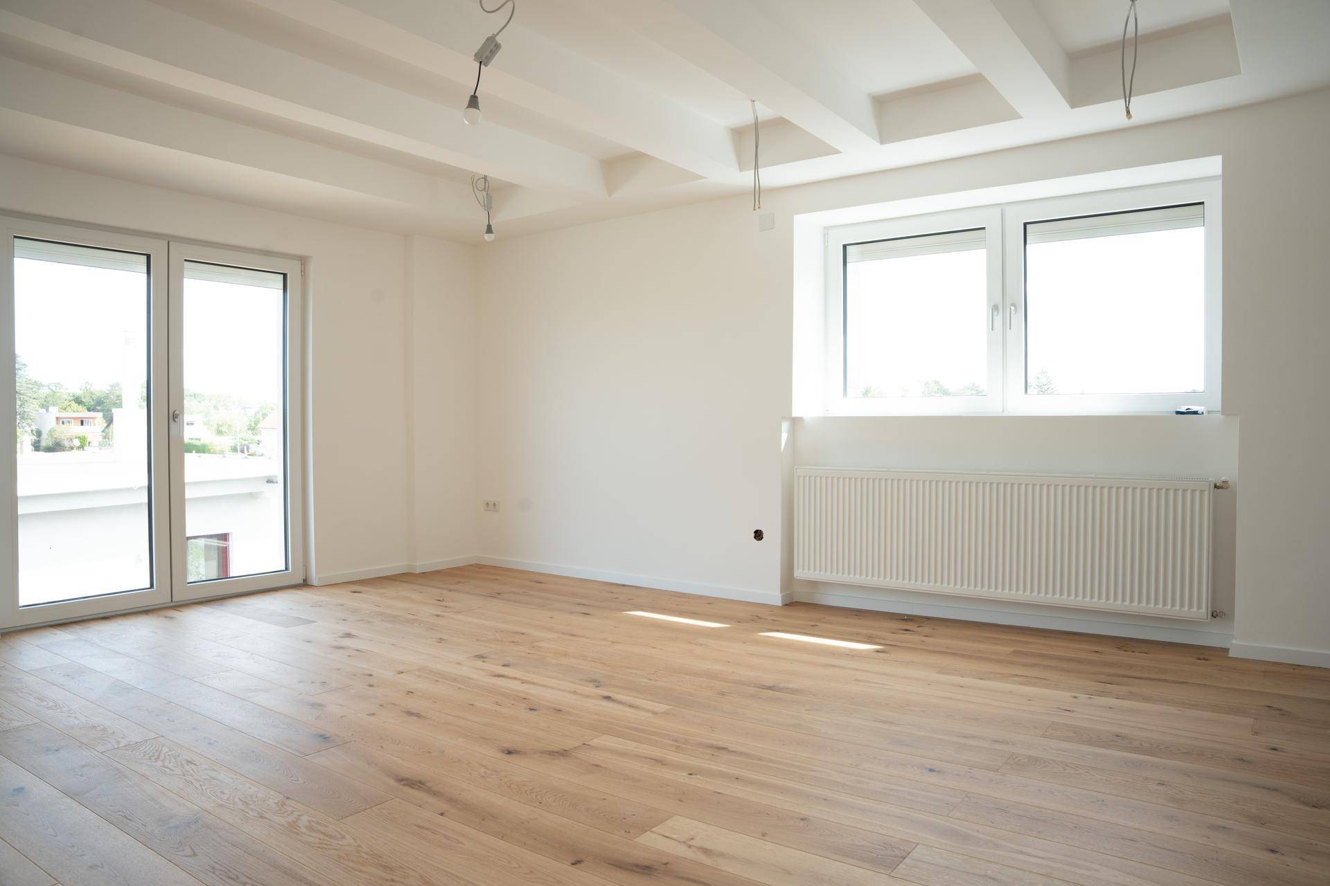 Heller Raum mit Holzboden, großen Fenstern und Zugang zu einem Außenbereich.