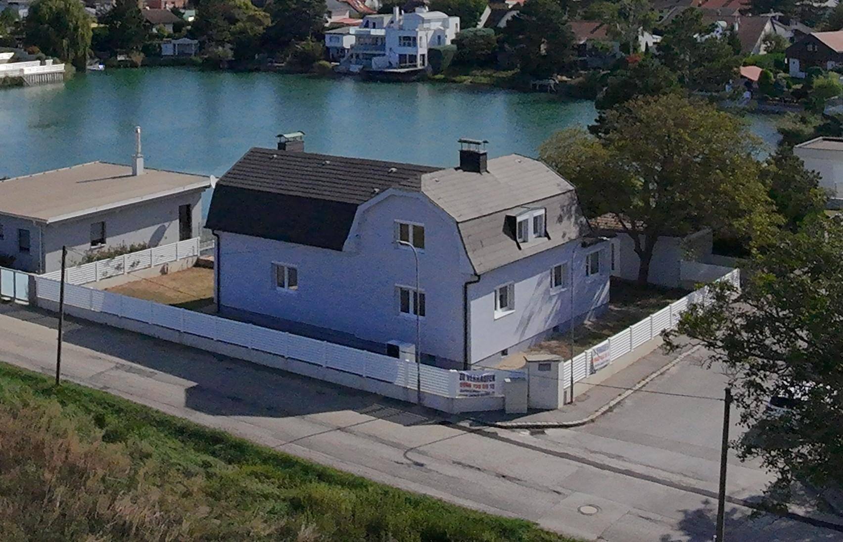 Luftaufnahme des Hauses am See mit umliegenden Grundstücken und Straße.