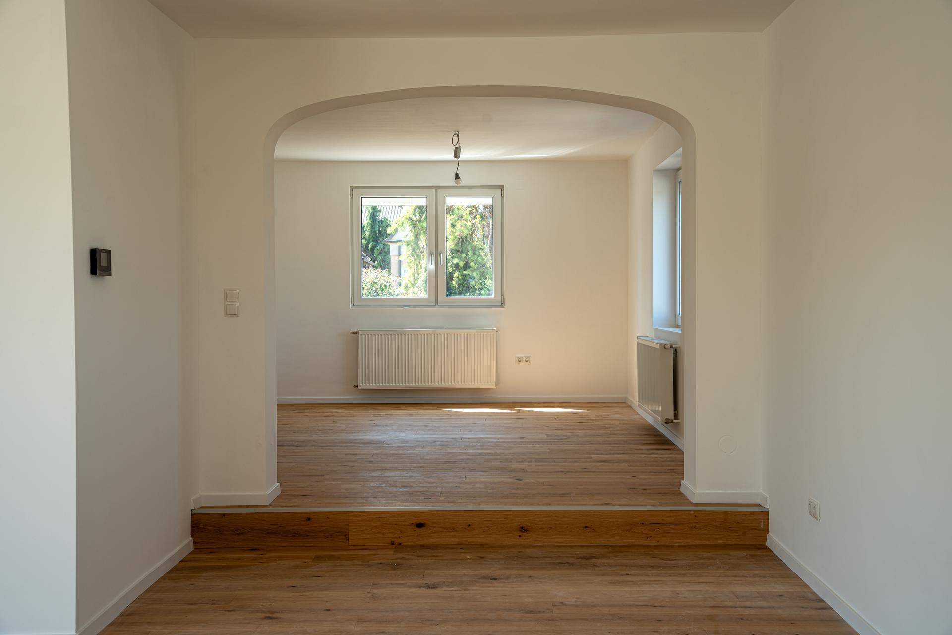 Geräumiger Wohnbereich mit Holzboden und natürlichem Lichteinfall durch Fenster.